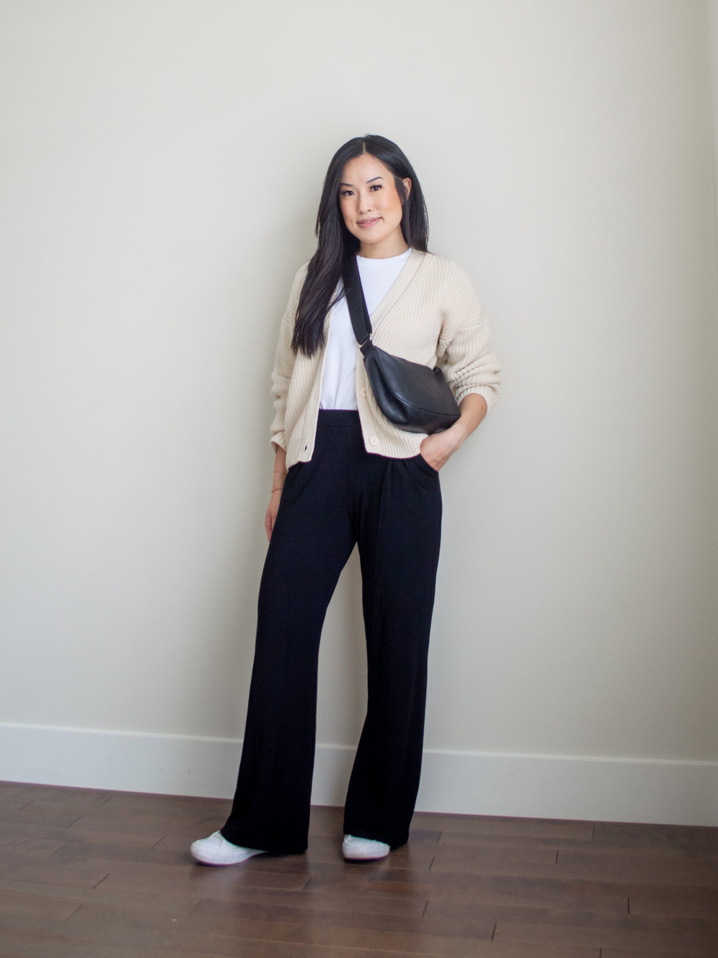 Sharon of Her Simple Sole is showcasing a t-shirt outfit for fall, featuring a simple white T-shirt, cream cotton cardigan, black wide-leg pants, a black slouchy bag and a pair of monochrome white Converse sneakers | minimalist outfits | fall outfit ideas