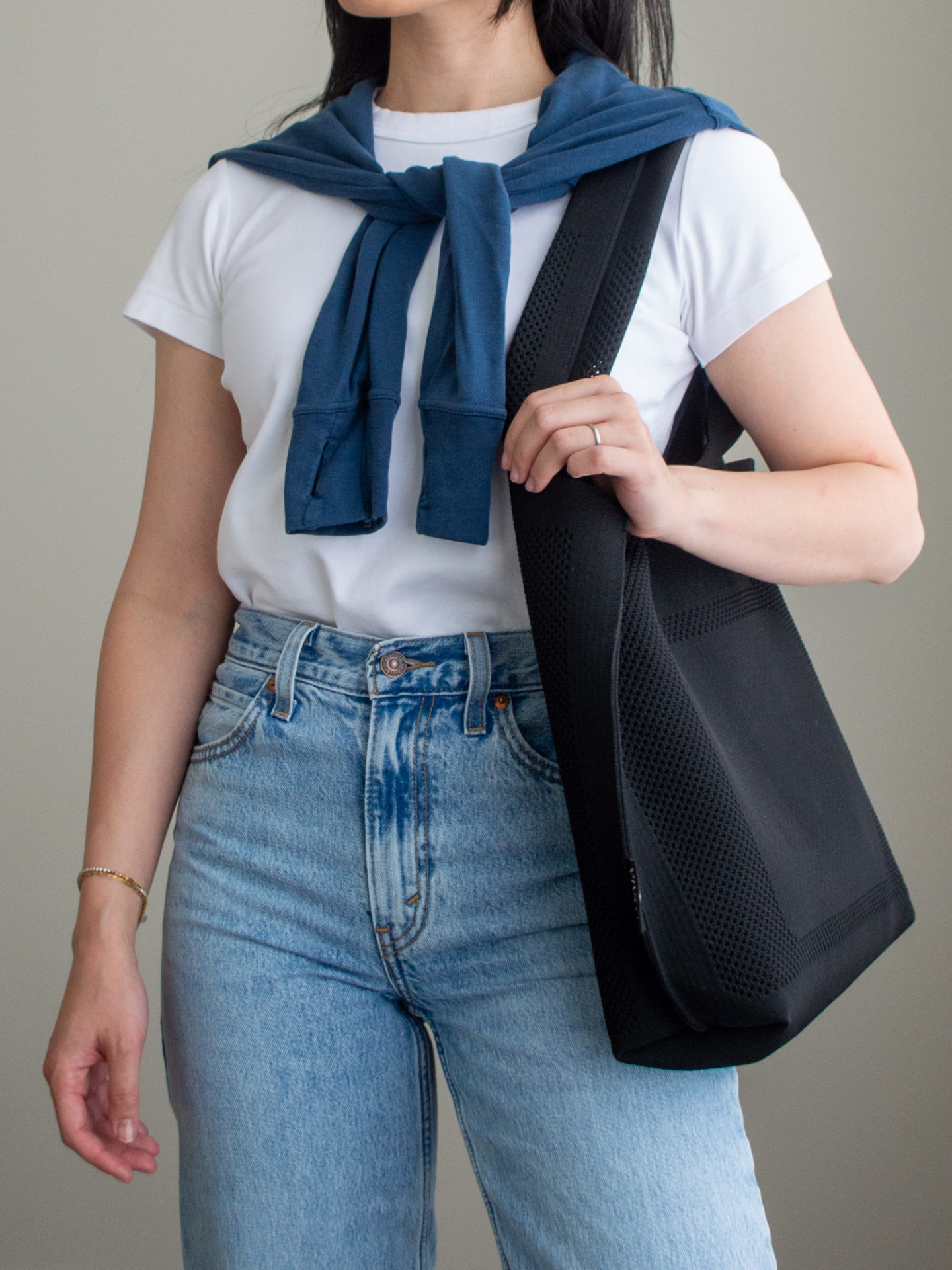 Close-up detailed outfit shot of Sharon of Her Simple Sole wearing a simple white T-shirt, a blue sweatshirt tied over the shoulder, a pair of wide-leg jeans, and a black tote bag | minimalist outfits | fall outfit ideas