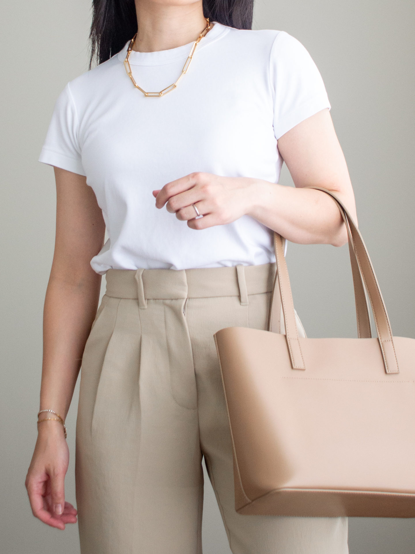 Close-up detailed outfit shot of Sharon of Her Simple Sole wearing a simple white T-shirt, a chunky gold chain necklace, camel coloured tailored trousers, and a caramel mini tote bag | minimalist outfits | fall outfit ideas