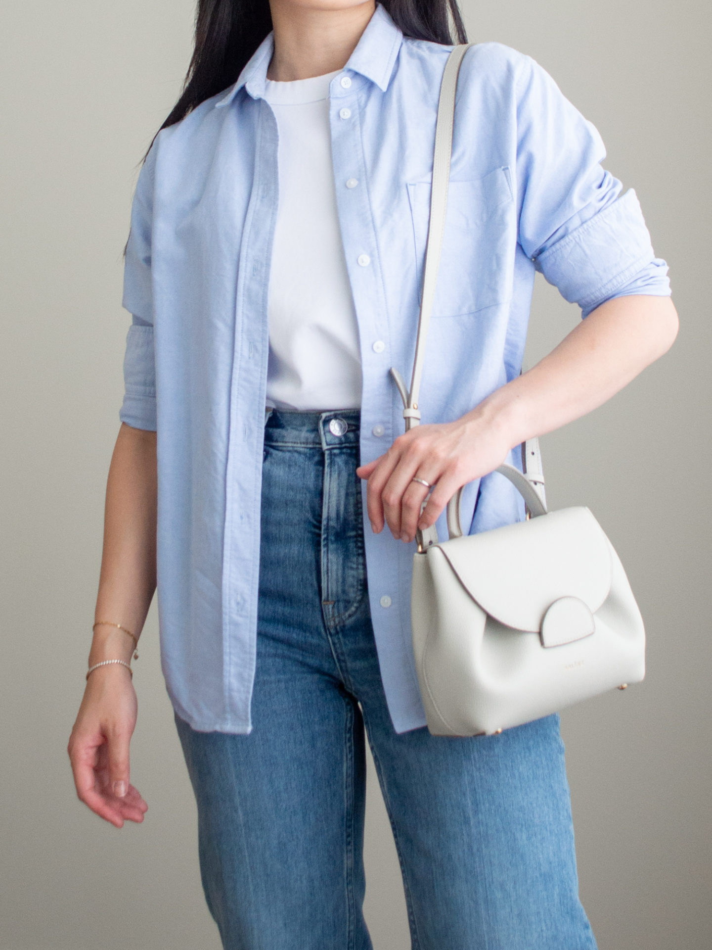 Close-up detailed outfit shot of Sharon of Her Simple Sole wearing a simple white T-shirt, a blue relaxed button up shirt, a pair of blue straight leg jeans, and an off-white crossbody bag | minimalist outfits | fall outfit ideas