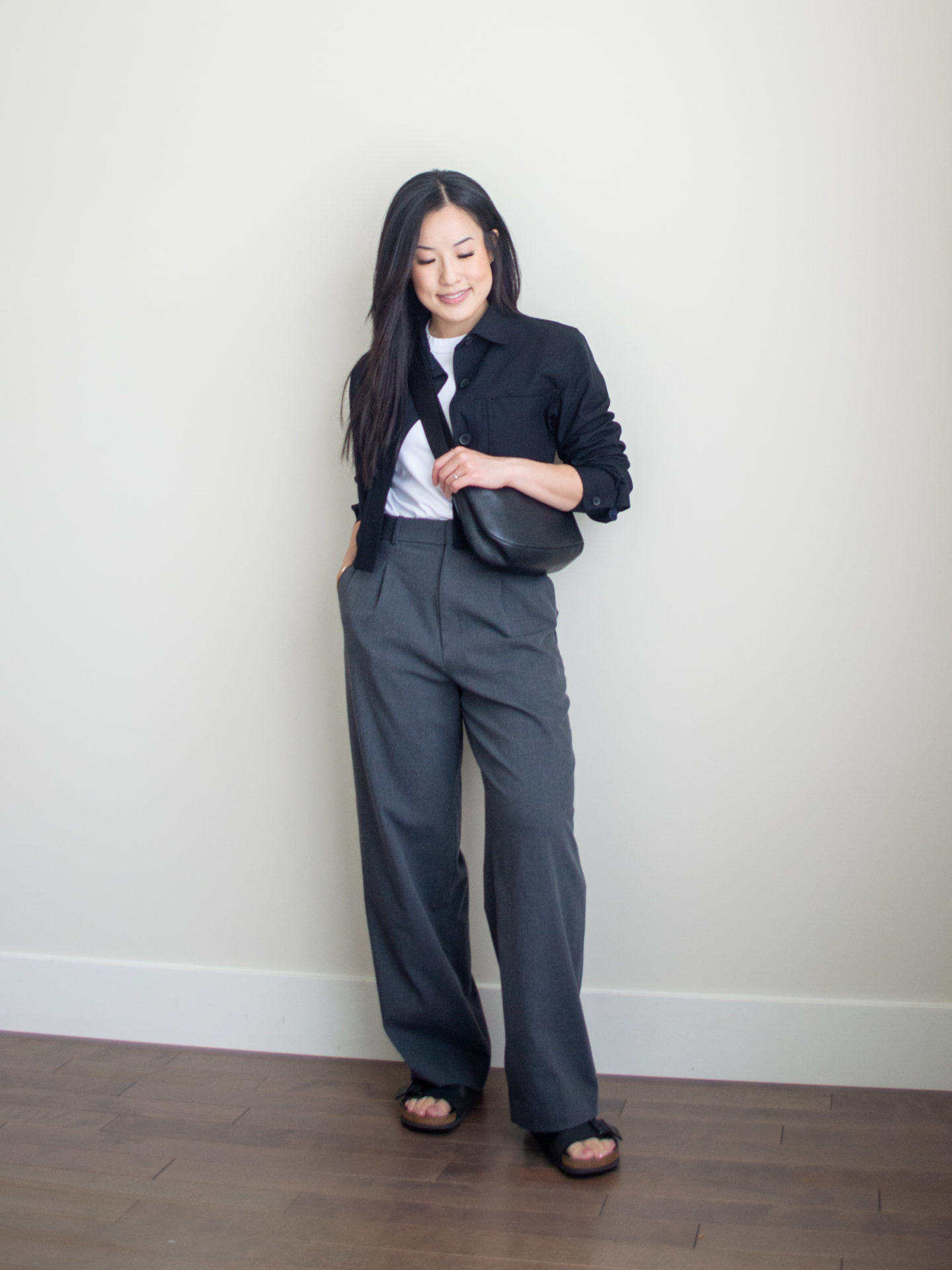 Sharon of Her Simple Sole is showcasing a t-shirt outfit for fall, featuring a simple white T-shirt, a black cropped jacket, a pair of grey wide-leg pants, a black slouchy bag and a pair of buckle sandals | minimalist outfits | fall outfit ideas