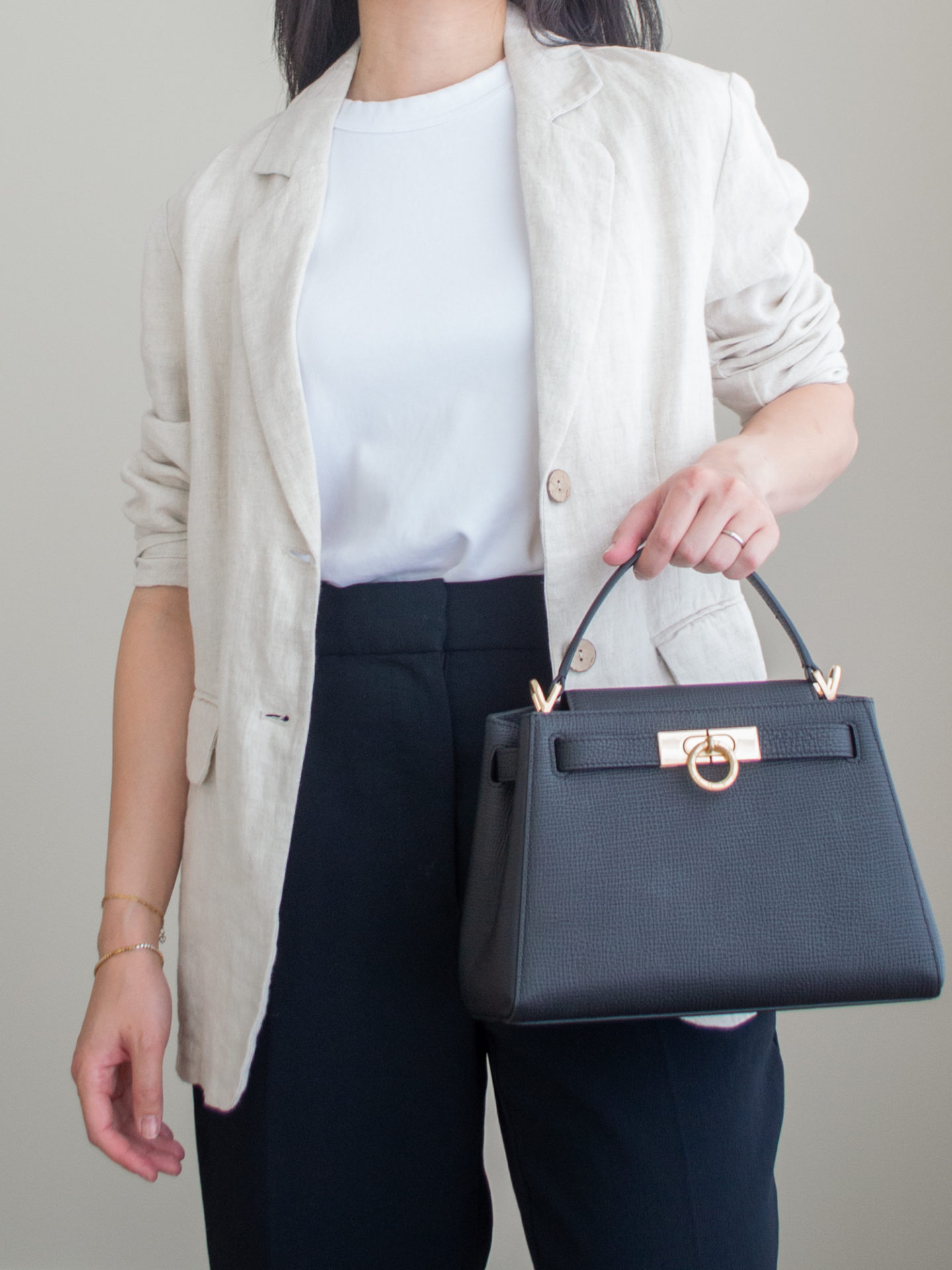 Close-up detailed outfit shot of Sharon of Her Simple Sole wearing a white T-shirt featuring a simple white T-shirt, a cream linen blazer, a pair of black wide-leg pants, and a black top handle bag | minimalist outfits | fall outfit ideas