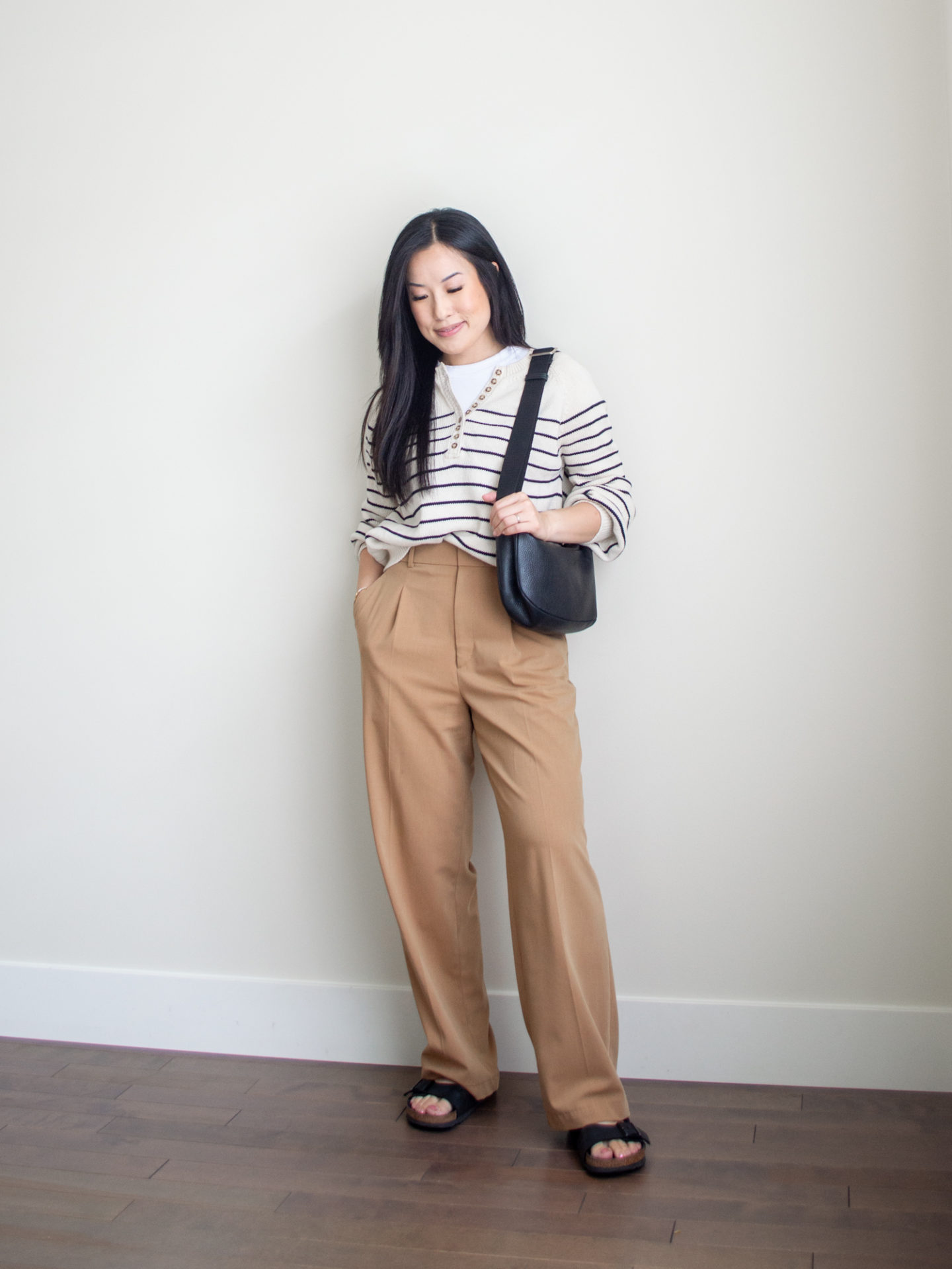 Sharon of Her Simple Sole is showcasing a t-shirt outfit for fall, featuring a simple white T-shirt, a striped cotton sweater, brown wide-leg pants, a black slouchy bag and buckle sandals | minimalist outfits | fall outfit ideas