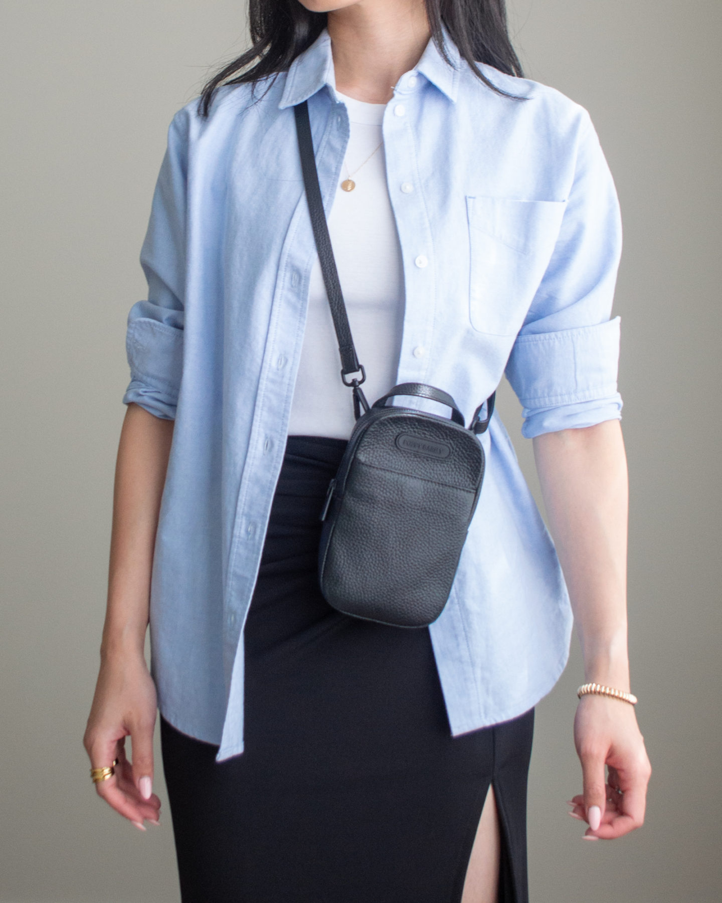 Close-up detailed outfit shot of Sharon of Her Simple Sole wearing a basic ribbed tank top, a blue relaxed oxford button up shirt and a black midi skirt while wearing a black crossbody mini bag | minimalist outfits | summer outfit ideas | button up shirt outfit