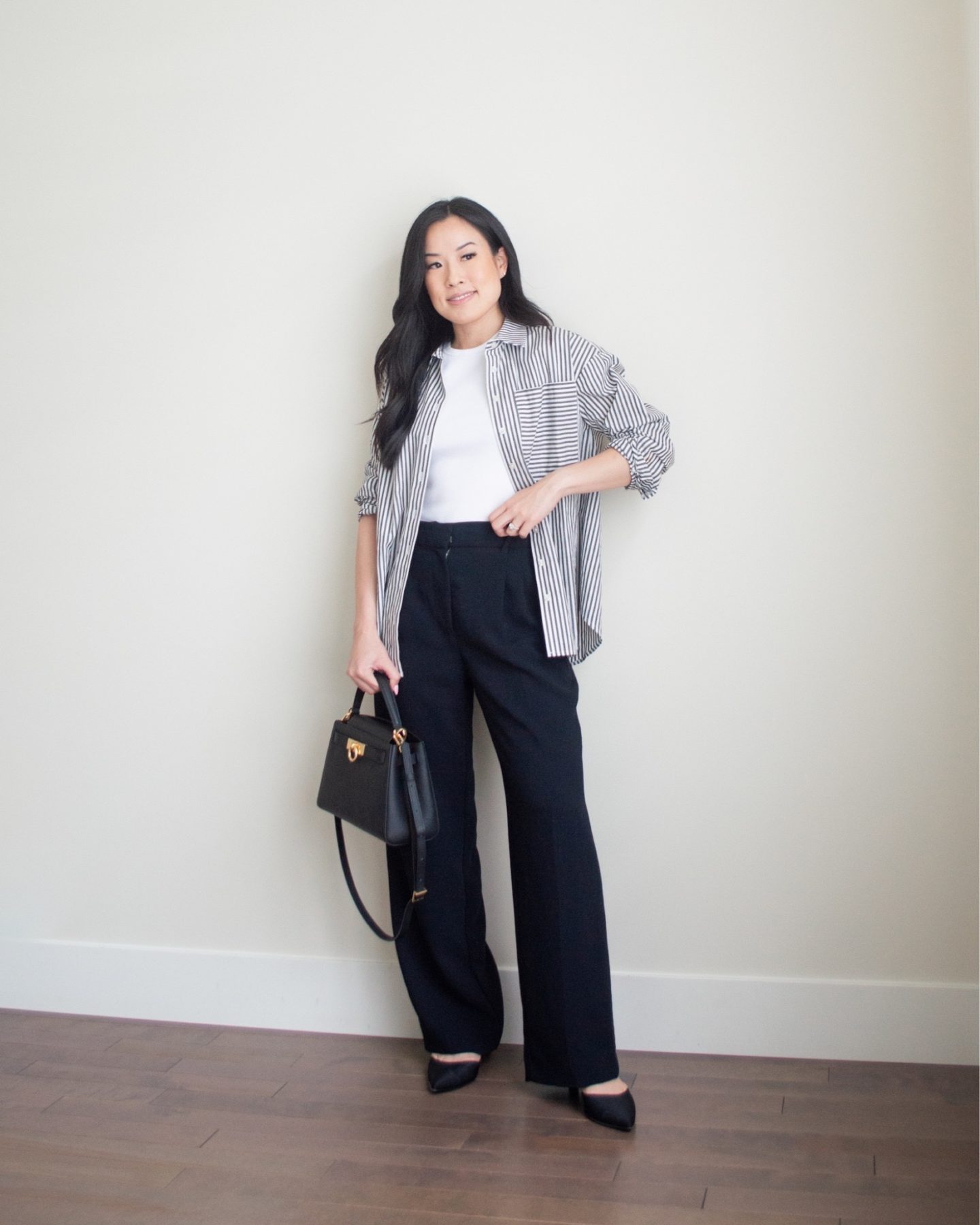 Sharon of Her Simple Sole is showcasing an outfit from her July outfit roundup, featuring a striped button up shirt, a baby t-shirt, and black wide leg pants, while holding a black top handle bag and wearing a pair of pointy toe sling back kitten heels | minimalist outfits | summer outfit ideas | wide leg pants outfit