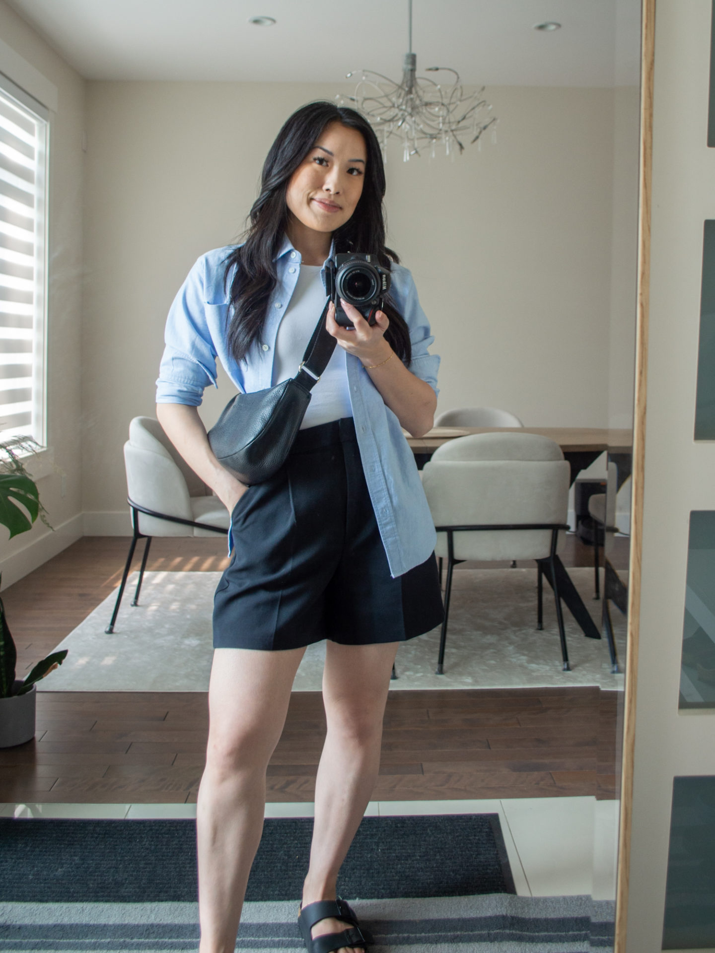 Sharon of Her Simple Sole is showcasing an outfits using simple pieces that make deciding what to pack easy, featuring a white seamless bodysuit, a blue relaxed shirt, black tailored shorts, a black slouchy bag and buckle sandals | minimalist outfits | simple outfit ideas