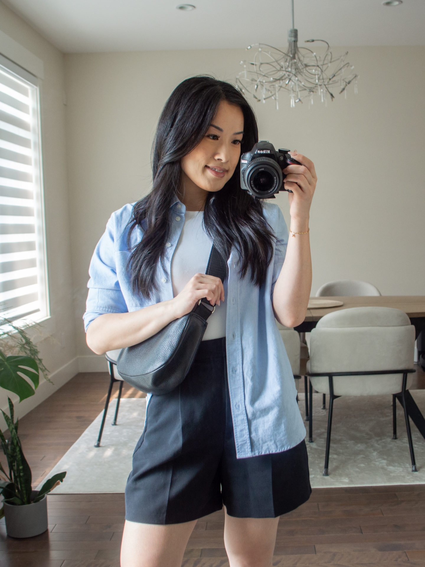 Close-up detailed outfit shot of Sharon of Her Simple Sole wearing a white seamless bodysuit, a blue relaxed shirt, black tailored shorts, and a black slouchy bag | minimalist outfits | simple outfit ideas | a week of outfits