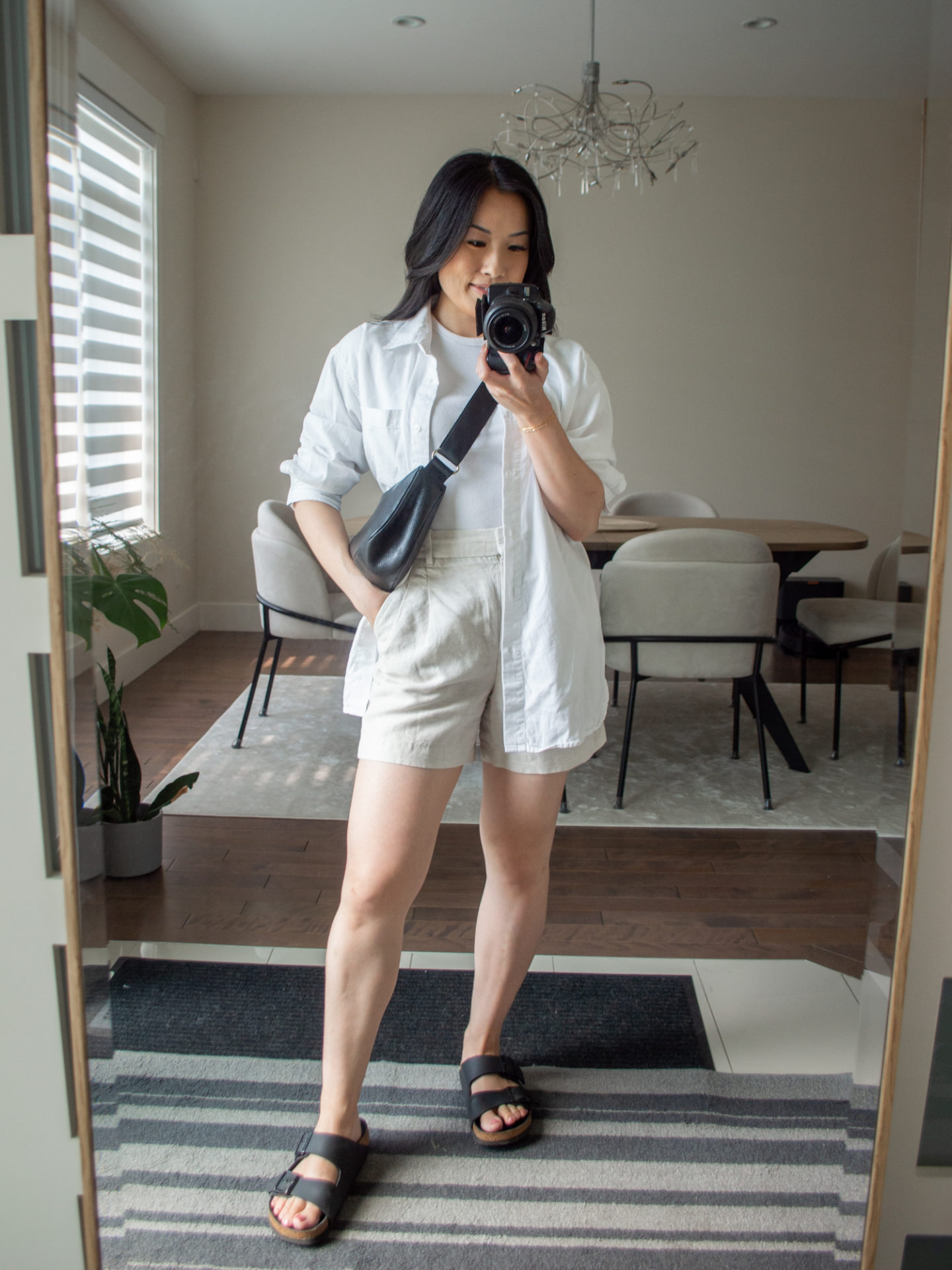 Sharon of Her Simple Sole is showcasing an outfits using simple pieces that make deciding what to pack easy, featuring a white baby T-Shirt, a white oversized button up shirt, cream linen shorts, a black slouchy bag and black buckle sandals | minimalist outfits | simple outfit ideas