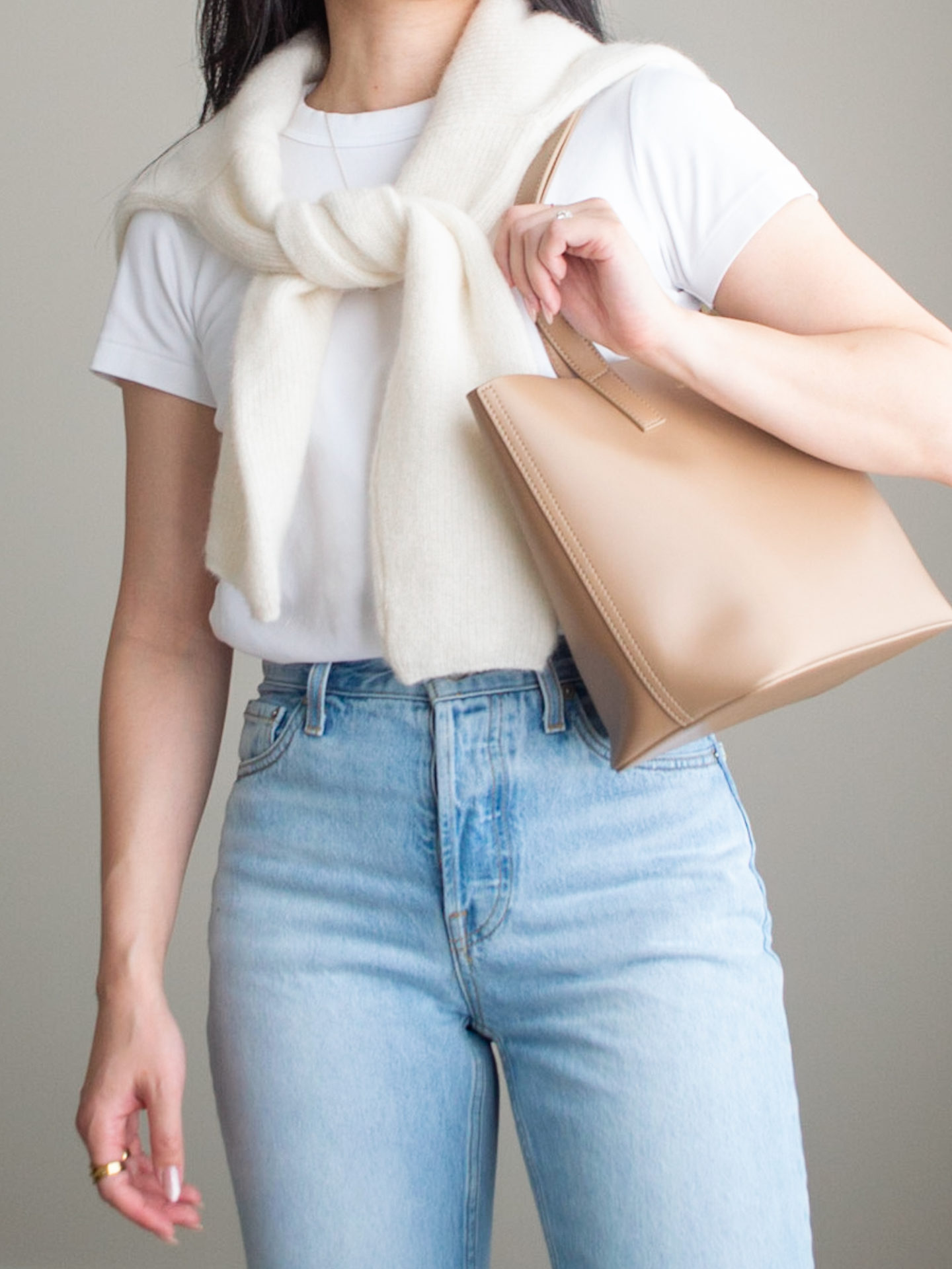 Close-up detailed outfit shot of Sharon of Her Simple Sole wearing a basic white T-Shirt, blue straight leg jeans, a wool cardigan over the shoulders, and a caramel mini tote bag | minimalist outfits | simple outfit ideas