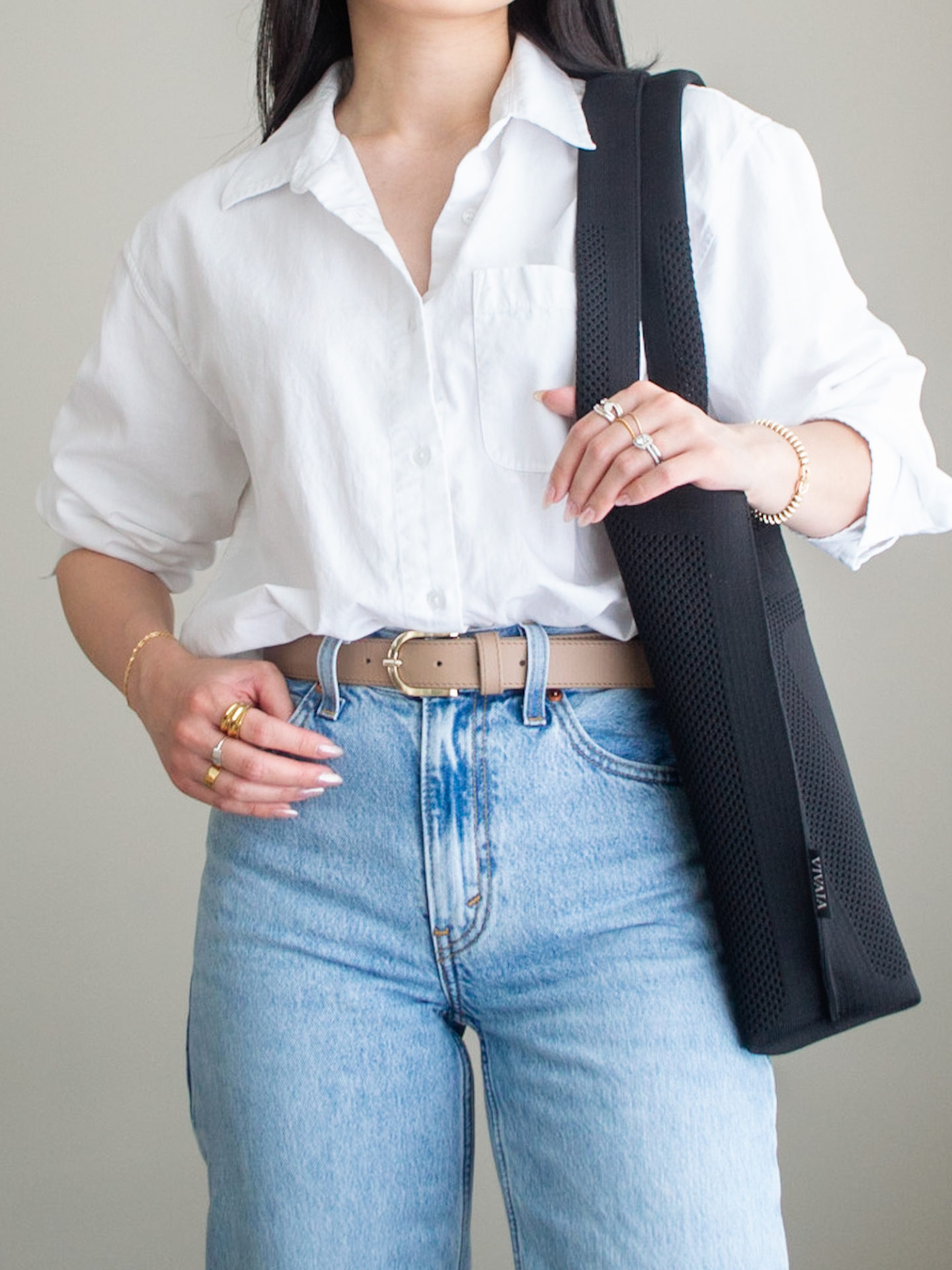 Close-up detailed outfit shot of Sharon of Her Simple Sole wearing a white oversized button up shirt, relaxed 90's jeans, a black tote bag, a neutral toned belt, and mixing silver and gold statement jewelry | minimalist outfits | simple outfit ideas