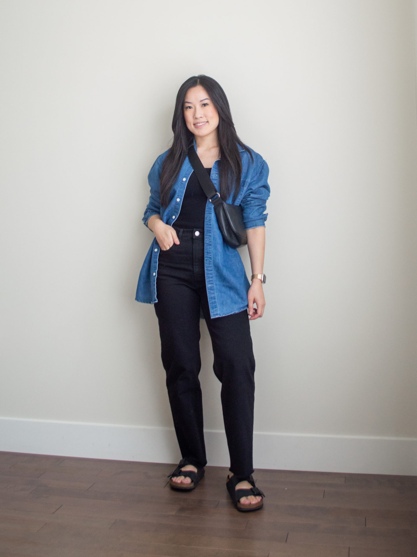 Sharon of Her Simple Sole is showcasing a outfit wearing one of her new Everlane staples, featuring a black square neck tank top, an oversized denim shirt with a pair of black straight leg jeans, a black slouchy bag and a pair of buckle sandals | minimalist outfits | simple outfit ideas