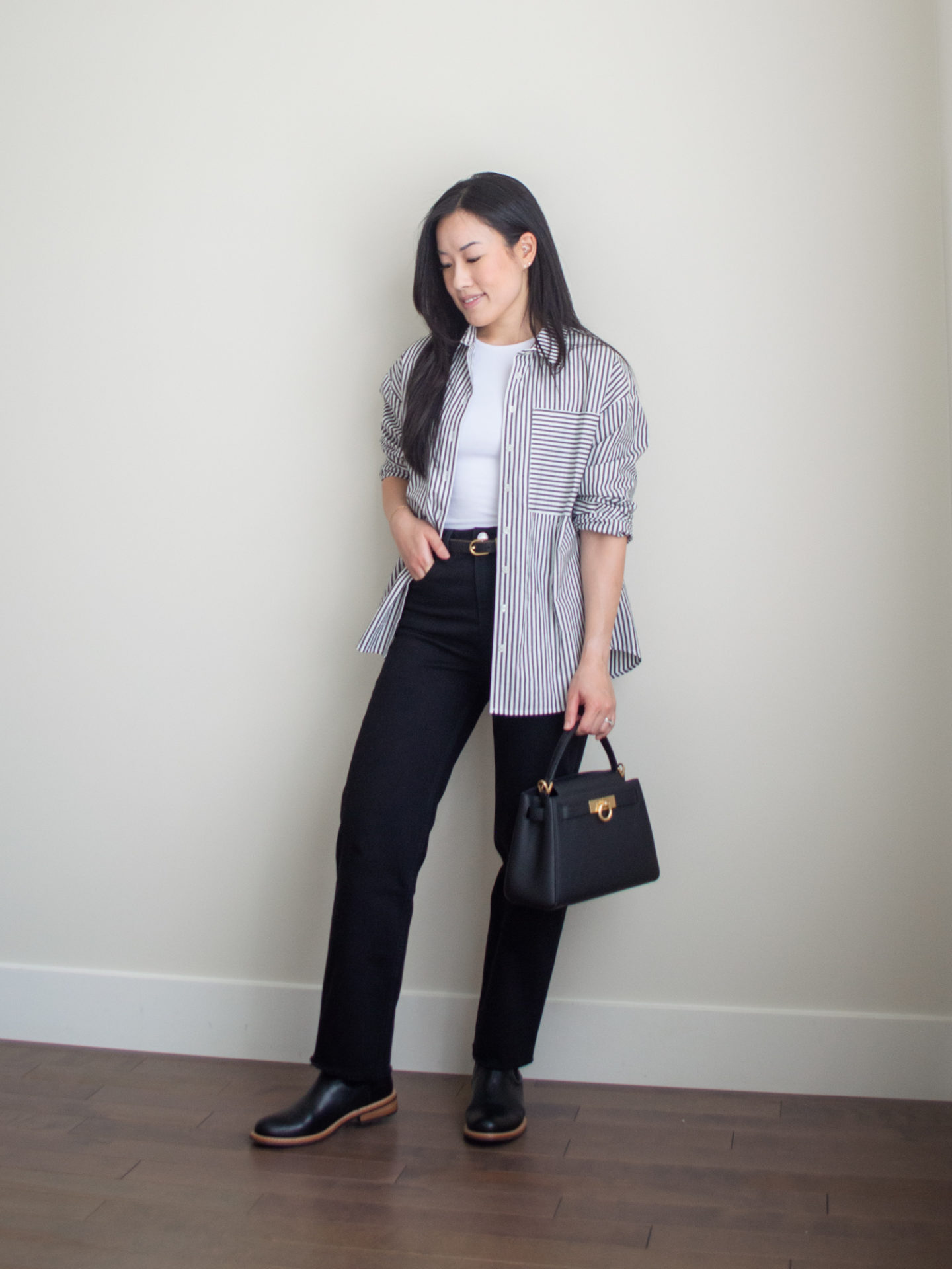 Sharon of Her Simple Sole is showcasing a outfit wearing one of her new Everlane staples, featuring a striped button up shirt, a baby t-shirt, black straight leg jeans, a black top handle bag and black boots | minimalist outfits | simple outfit ideas