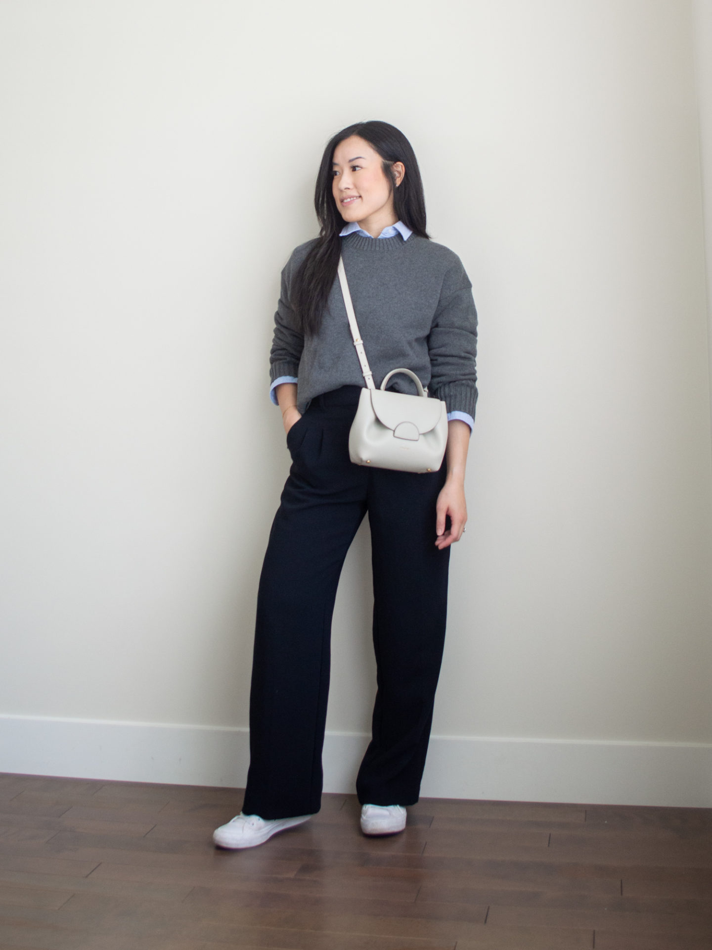 Sharon of Her Simple Sole is showcasing a outfit wearing one of her new Everlane staples, featuring a grey sweater, a blue relaxed button up shirt, black wide-leg pants, an off-white crossbody bag and white sneakers | minimalist outfits | simple outfit ideas