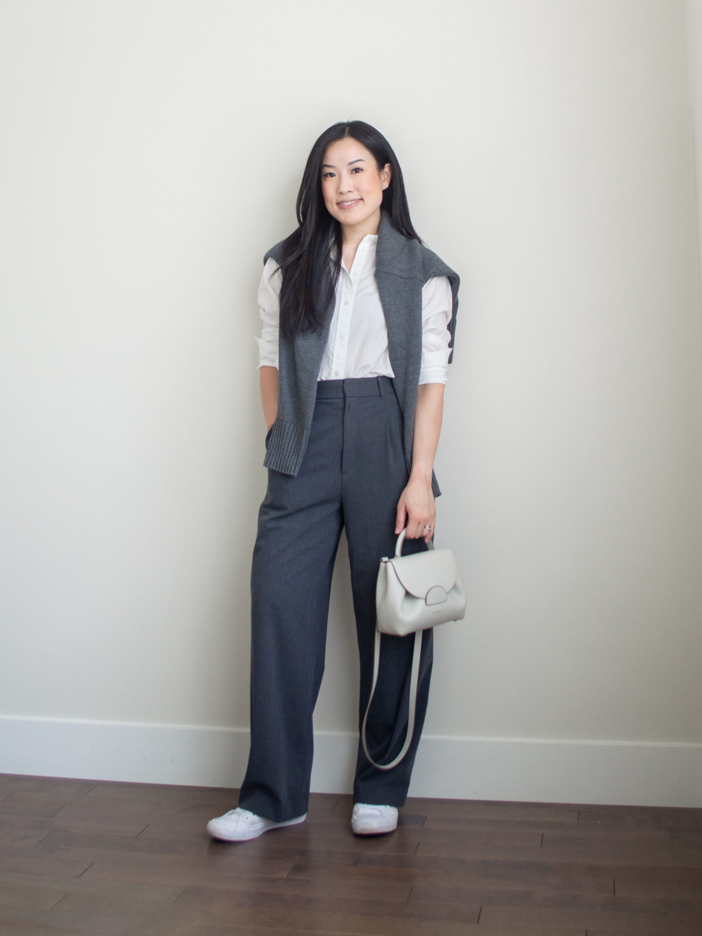 Sharon of Her Simple Sole is showcasing a outfit wearing one of her new Everlane staples, featuring a white linen button up shirt, a grey sweater, grey wide-leg pants, an off-white crossbody bag and white sneakers | minimalist outfits | simple outfit ideas