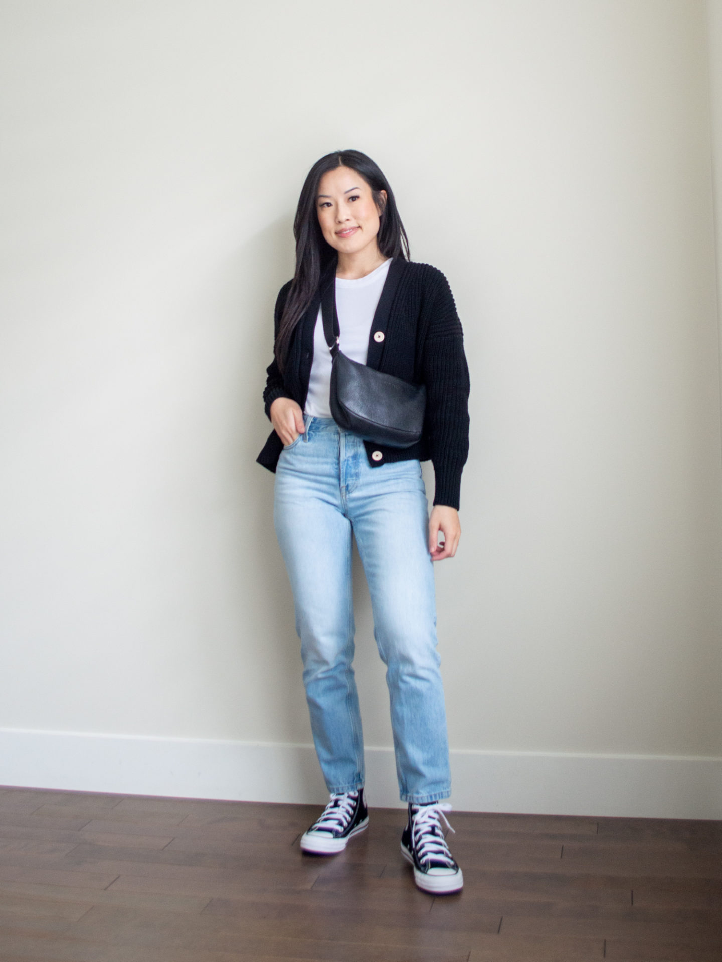 Sharon of Her Simple Sole is showcasing a outfit from her August outfit roundup, featuring a basic white tank top, a black cotton cardigan, a pair of blue straight-fit jeans, a black slouchy bag, and black Converse Chuck Taylor All Star sneakers | minimalist outfits | simple outfit ideas