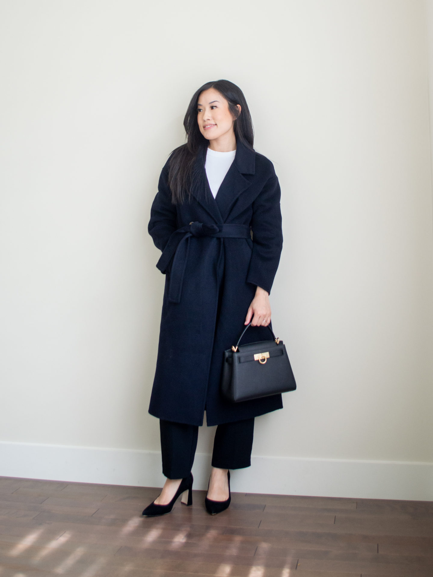 Sharon of Her Simple Sole is showcasing a outfit from her August outfit roundup, featuring featuring a basic white T-shirt, a long navy cashmere coat, black cropped trousers, a black top handle bag, and a pair of pointy toe pumps | minimalist outfits | simple outfit ideas