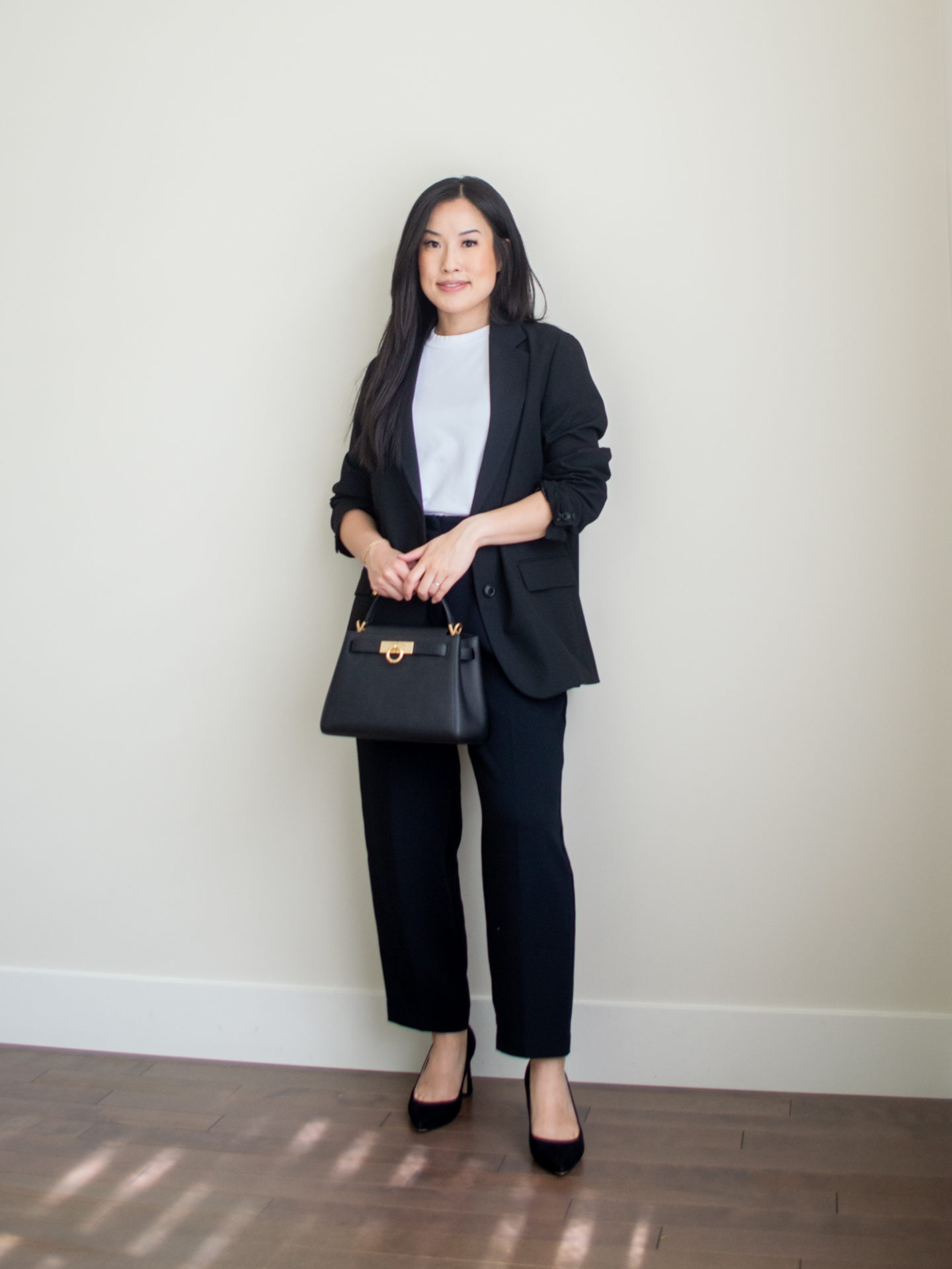 Sharon of Her Simple Sole is showcasing a outfit from her August outfit roundup, featuring a basic white T-shirt, a relaxed black blazer, black cropped trousers, a black top handle bag, and a pair of pointy toe pumps | minimalist outfits | simple outfit ideas