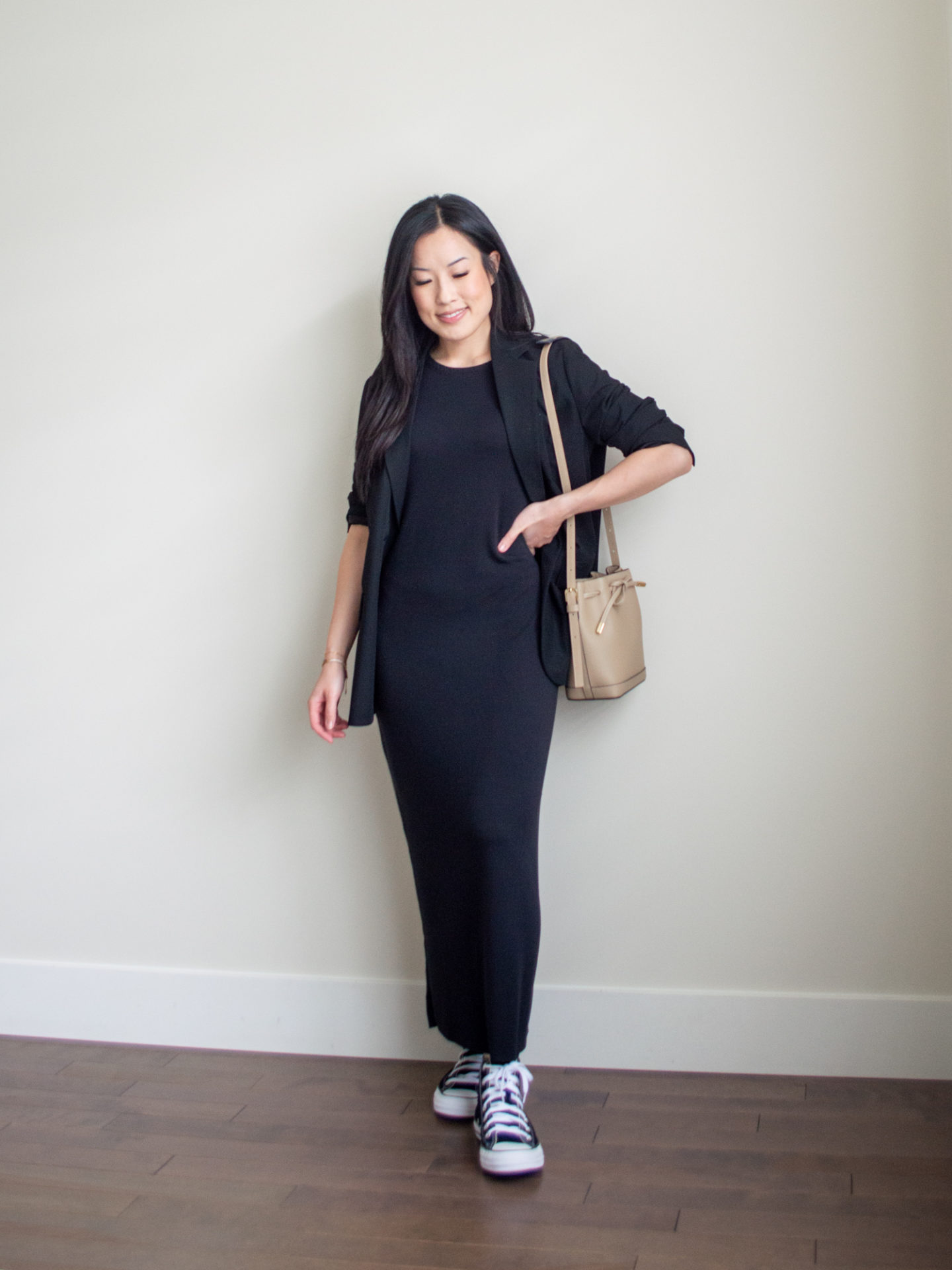 Sharon of Her Simple Sole is showcasing a outfit from her August outfit roundup, featuring a black maxi dress, a relaxed black blazer, a taupe bucket bag and black Converse Chuck Taylor All Star sneakers | minimalist outfits | simple outfit ideas