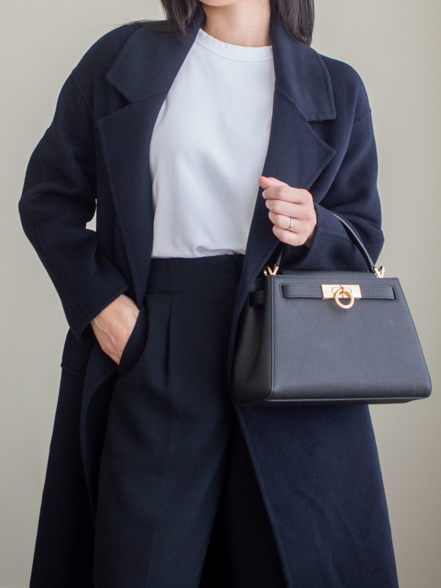 Close-up detailed outfit shot of Sharon of Her Simple Sole wearing a basic white T-shirt, a navy cashmere long coat, black cropped trousers, and a black top handle bag | minimalist outfits | simple outfit ideas