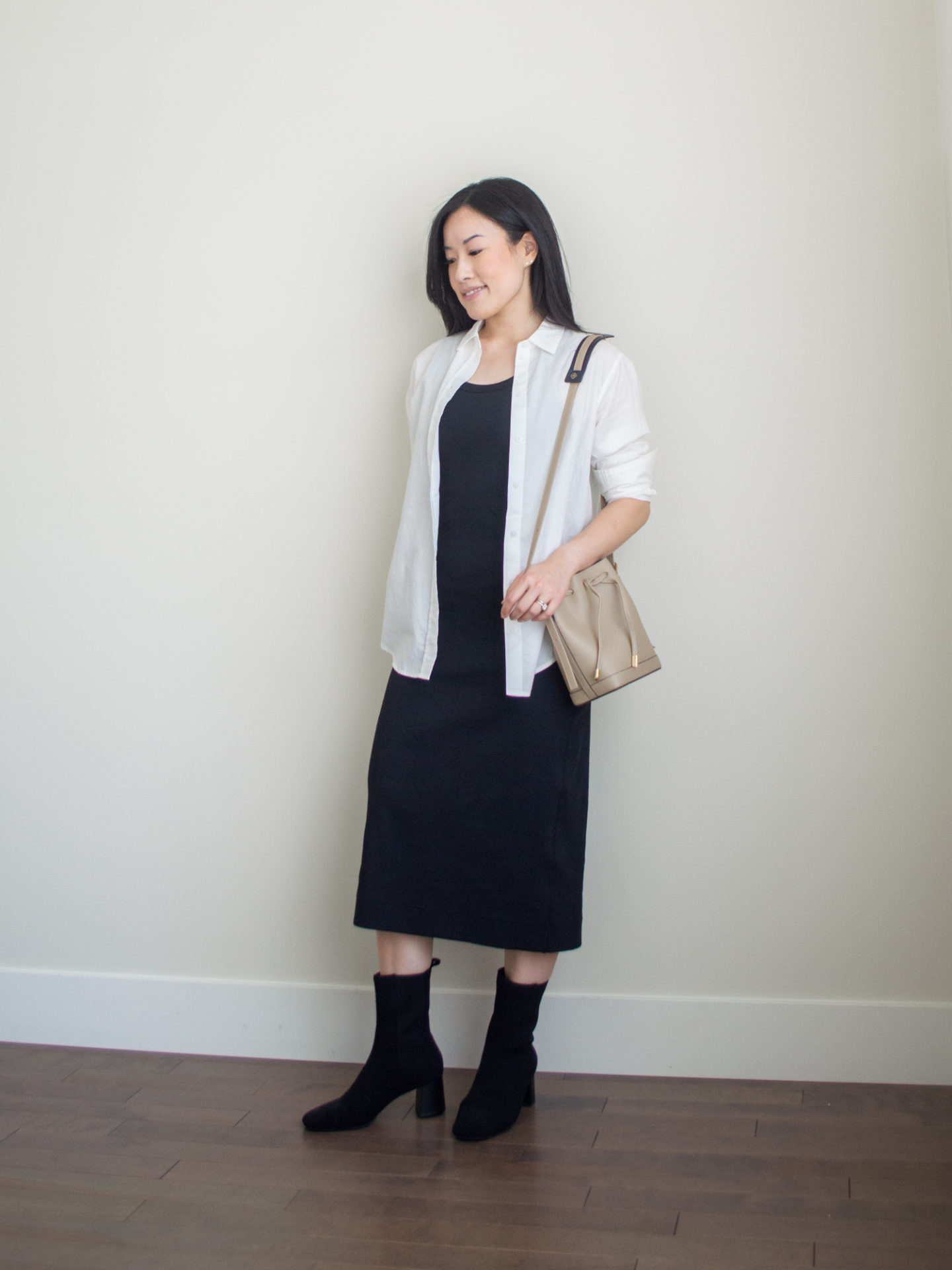 Sharon of Her Simple Sole is showcasing a outfit wearing one of her new Everlane staples, featuring a black midi dress, a white button up shirt, a taupe bucket bag and black boots | minimalist outfits | simple outfit ideas