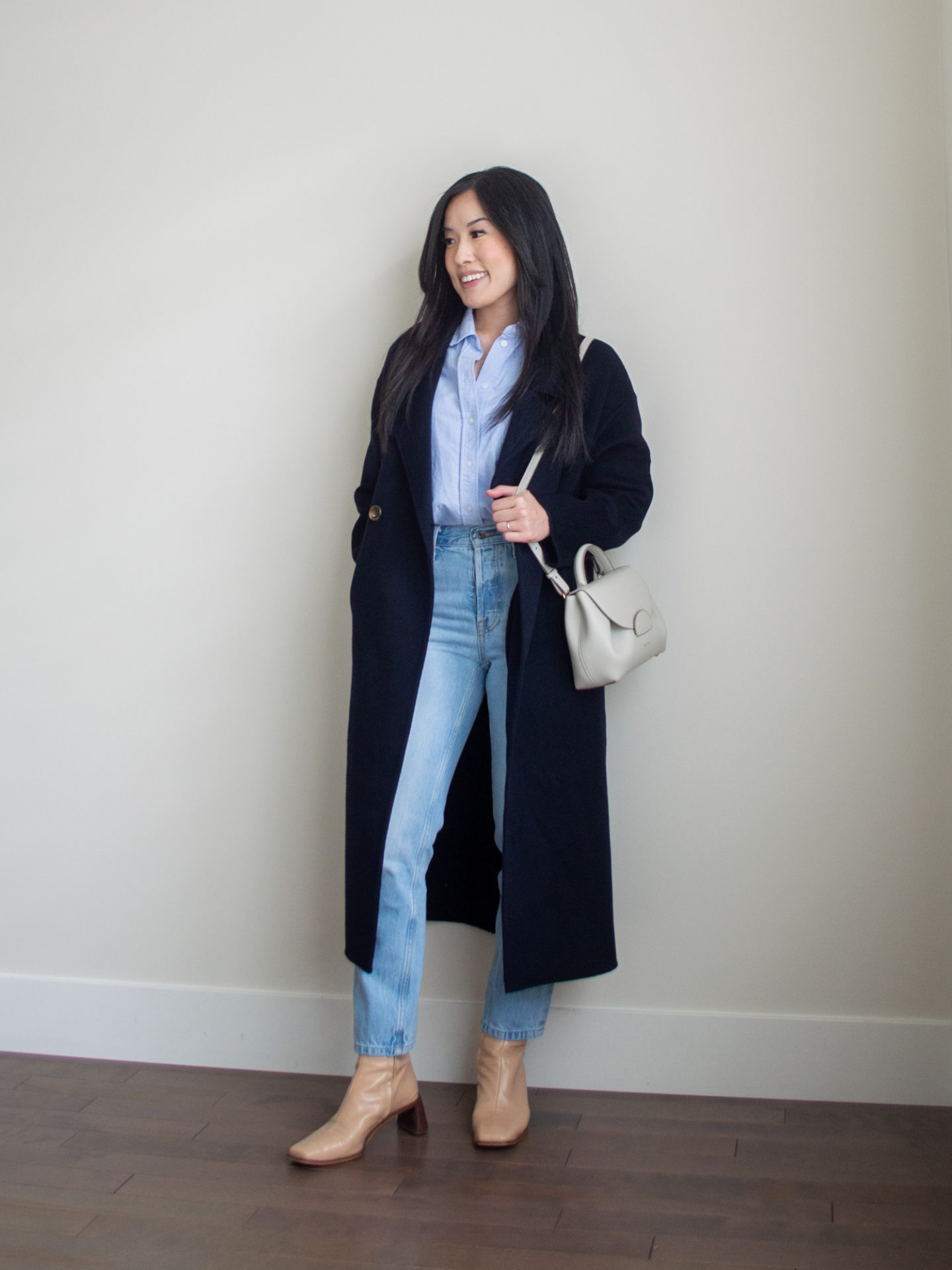 Sharon of Her Simple Sole is showcasing a outfit from her August outfit roundup, featuring a blue relaxed button up shirt, a navy cashmere coat, blue straight leg jeans, an off-white crossbody bag and nude ankle boots | minimalist outfits | simple outfit ideas