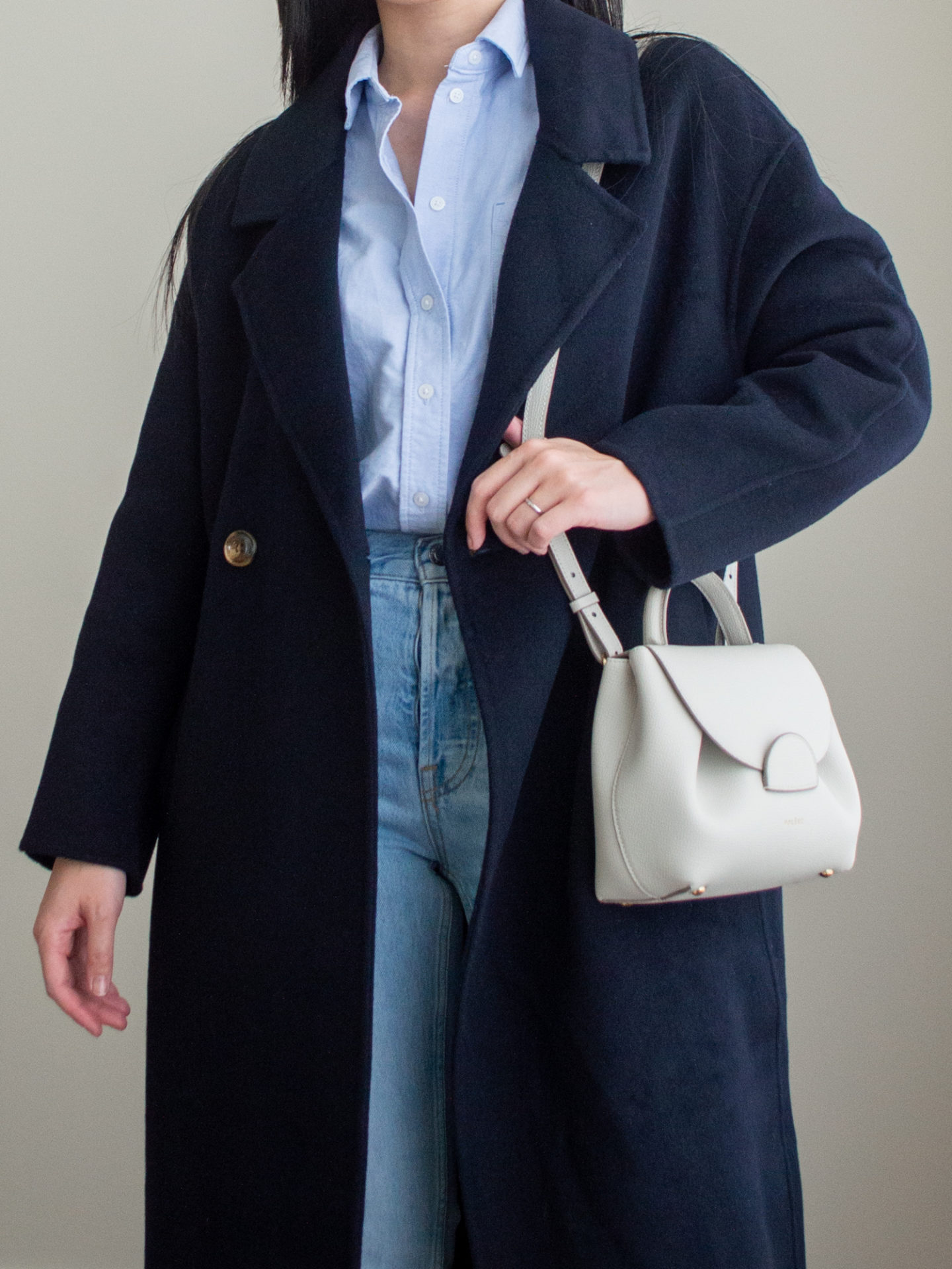 Close-up detailed outfit shot of Sharon of Her Simple Sole wearing a blue relaxed button up shirt, a navy cashmere coat, blue straight leg jeans, an off-white crossbody bag | minimalist outfits | simple outfit ideas