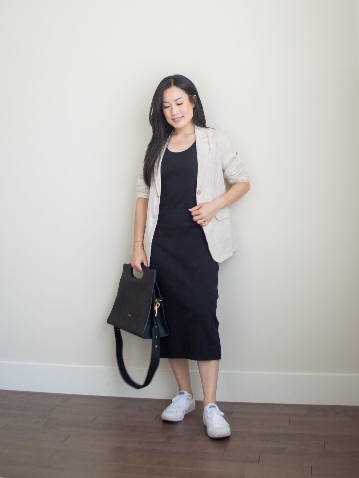 Sharon of Her Simple Sole is showcasing a outfit wearing one of her new Everlane staples, featuring a black midi dress, a linen blend blazer, a black briefcase-style bag and white sneaker | minimalist outfits | simple outfit ideas