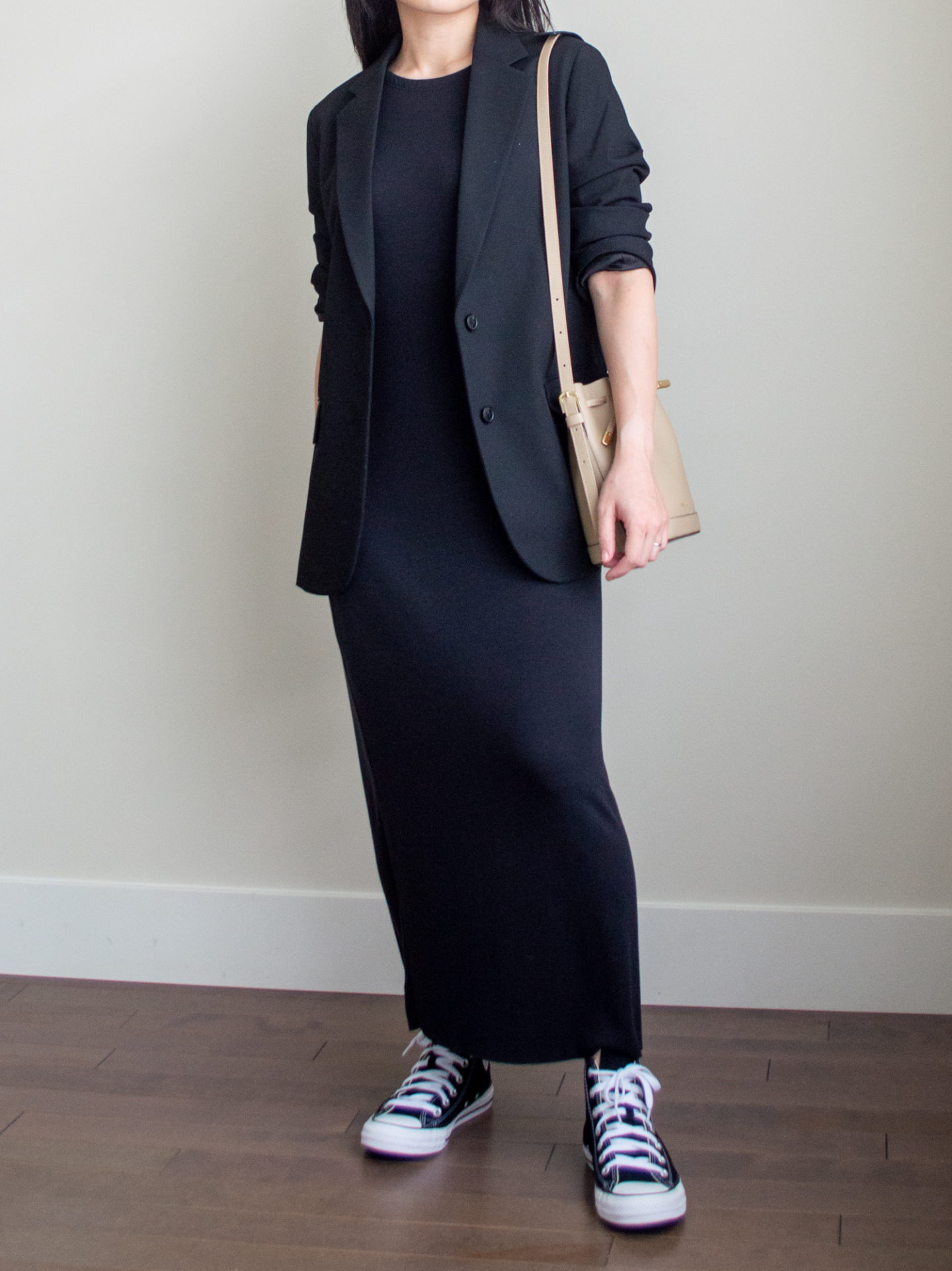 Close-up detailed outfit shot of Sharon of Her Simple Sole wearing a black maxi dress, a relaxed black blazer, a taupe bucket bag and a pair of black Converse Chuck Taylor All Star sneakers | minimalist outfits | simple outfit ideas