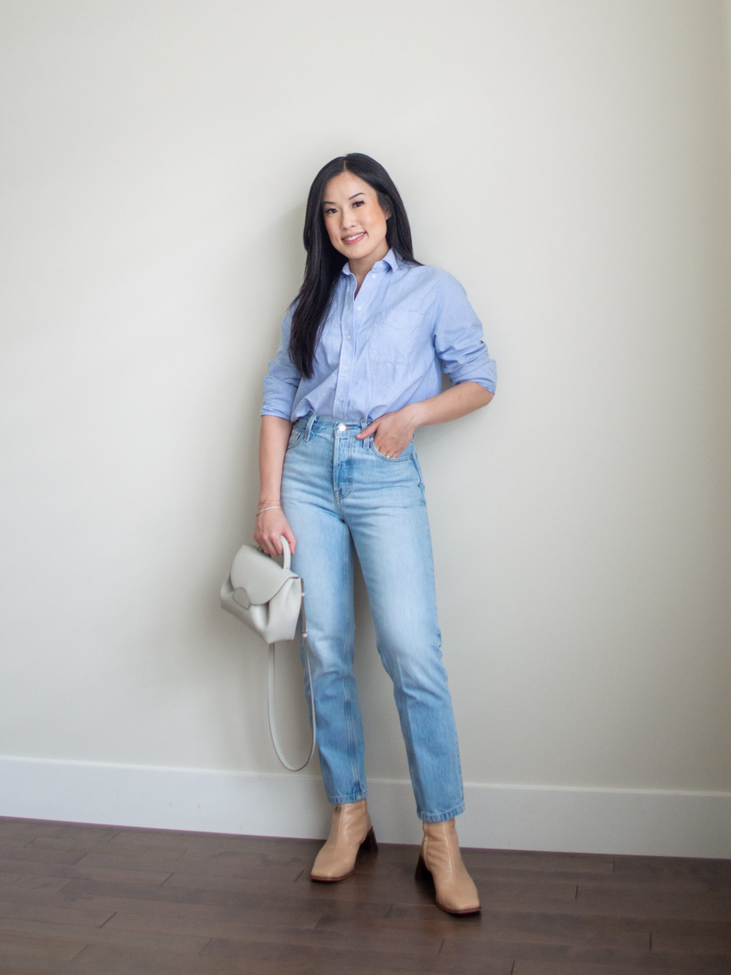 Sharon of Her Simple Sole is showcasing a outfit from her August outfit roundup, featuring a blue relaxed button up shirt, blue straight leg jeans, an off-white crossbody bag and a pair of nude ankle boots | minimalist outfits | simple outfit ideas