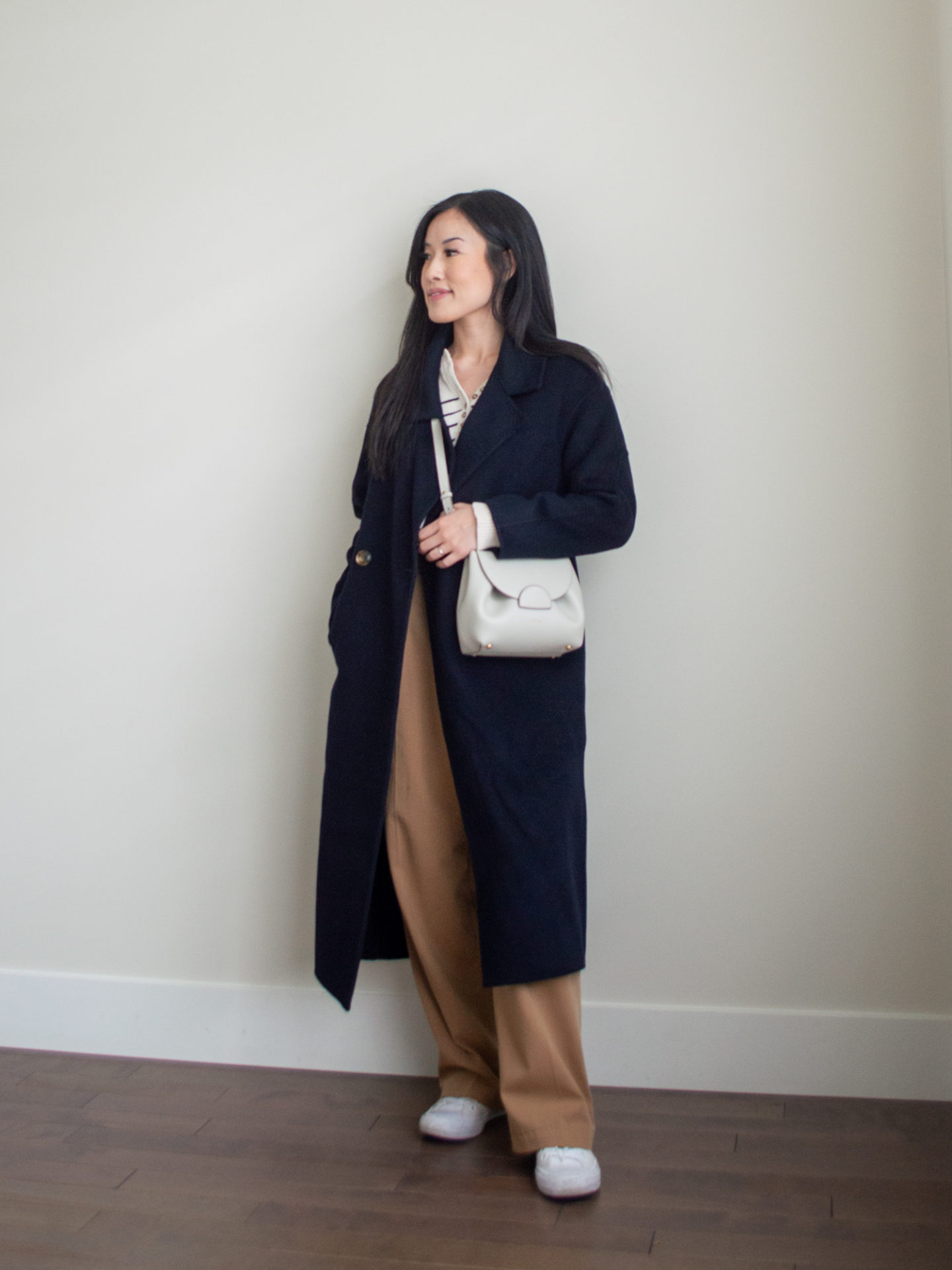 Sharon of Her Simple Sole is showcasing a outfit from her August outfit roundup, featuring a striped cotton sweater, a navy long cashmere coat, brown wide-leg pants, an off-white crossbody bag and white sneakers | minimalist outfits | fall outfit ideas