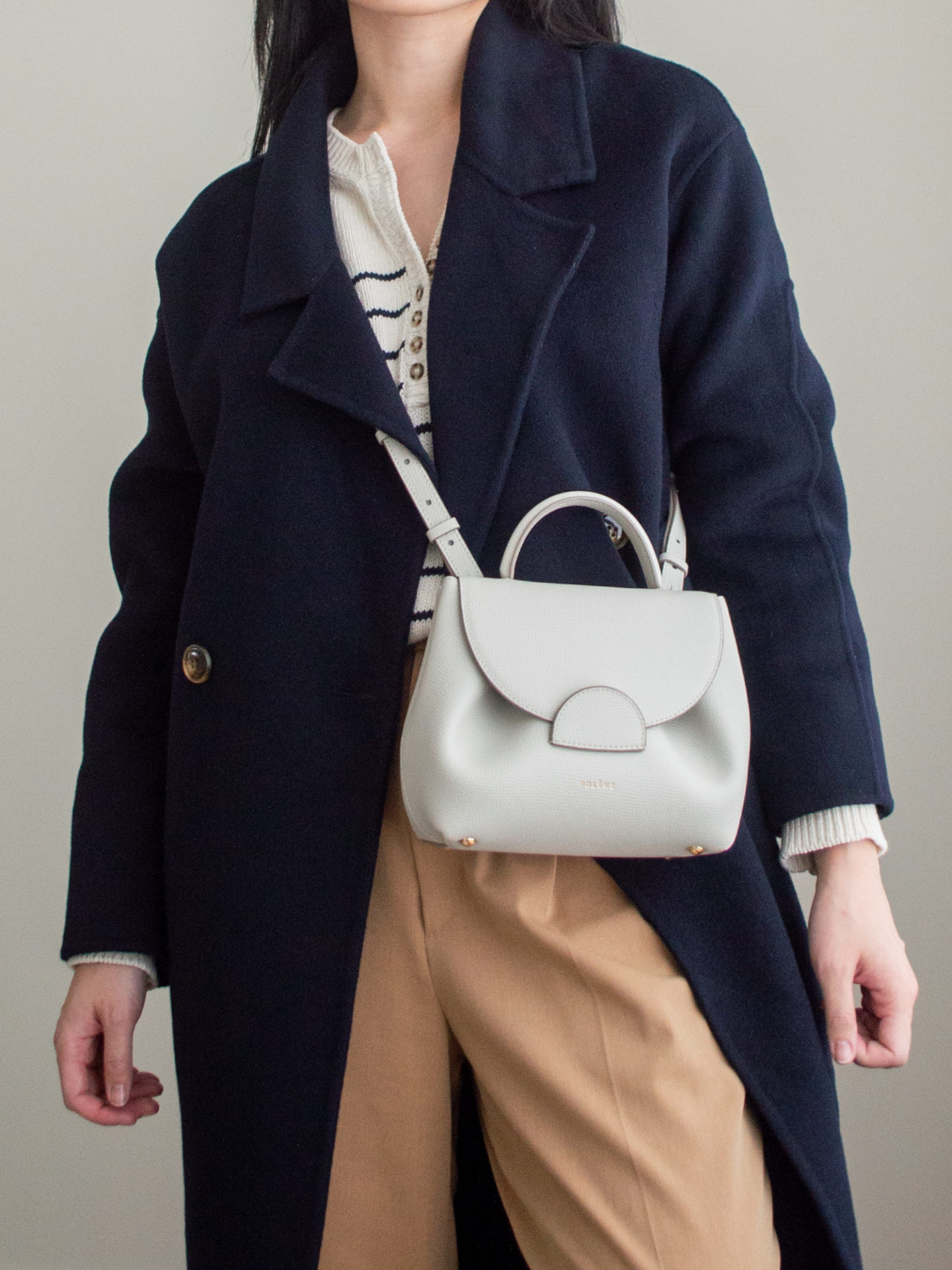 Close-up detailed outfit shot of Sharon of Her Simple Sole wearing a striped cotton sweater, a navy long cashmere coat, brown wide-leg pants, an off-white crossbody bag | minimalist outfits | simple outfit ideas