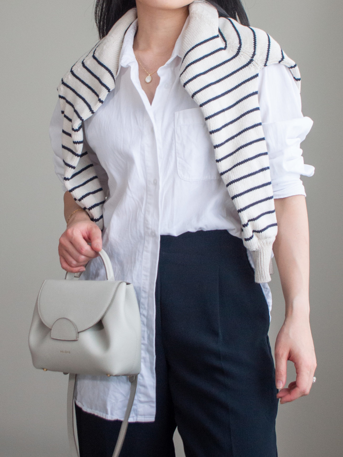 Close-up detailed outfit shot of Sharon of Her Simple Sole wearing an oversized white button-up shirt, striped sweater over the shoulder, black cropped pants, and an off-white crossbody bag | minimalist outfits | fall outfit ideas | simple outfit ideas