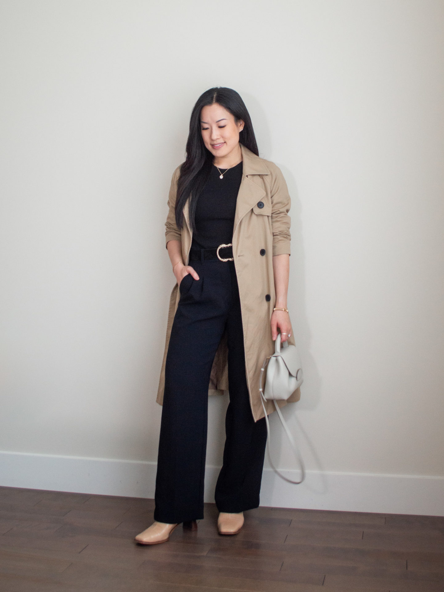 Sharon of Her Simple Sole is showcasing an outfit inspired by Parisian style, featuring a basic black long sleeve shirt, brown trench coat, black wide-leg pants, black statement belt, an off-white crossbody bag and nude ankle boots | minimalist outfits | fall outfit ideas | simple outfit ideas