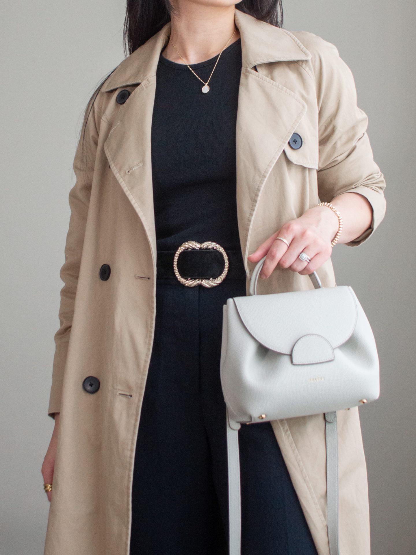 Close-up detailed outfit shot of Sharon of Her Simple Sole wearing a basic black long sleeve shirt, brown trench coat, black wide-leg pants, black statement belt and an off-white crossbody bag | minimalist outfits | fall outfit ideas | simple outfit ideas