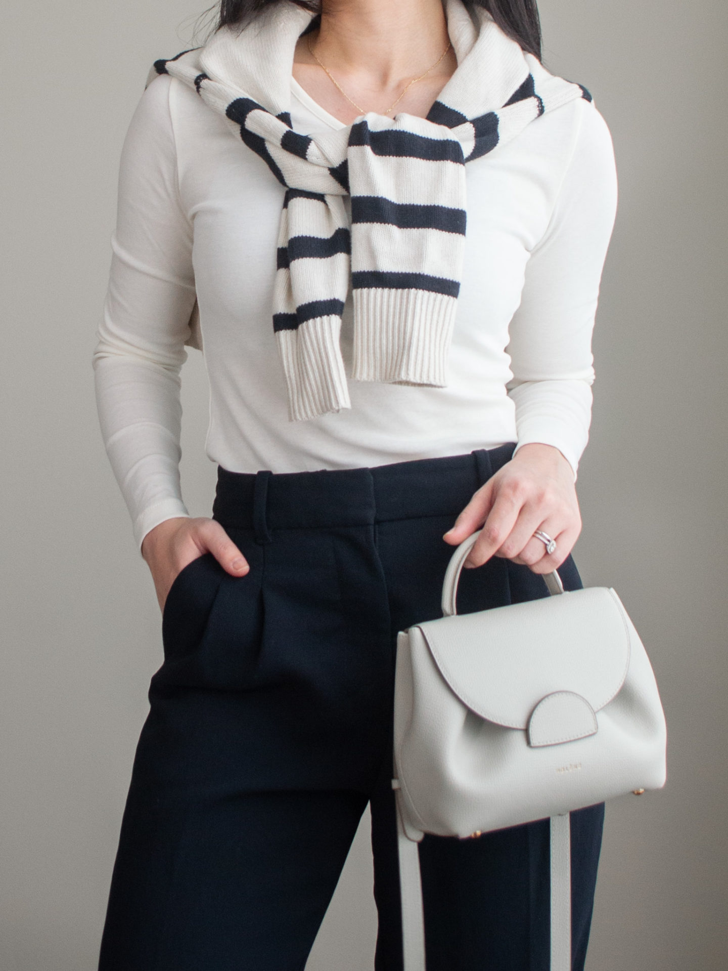 Close-up detailed outfit shot of Sharon of Her Simple Sole wearing a basic off-white long sleeve top, striped wool cardigan over the shoulder, black wide-leg pants, an off-white crossbody bag | minimalist outfits | fall outfit ideas | simple outfit ideas