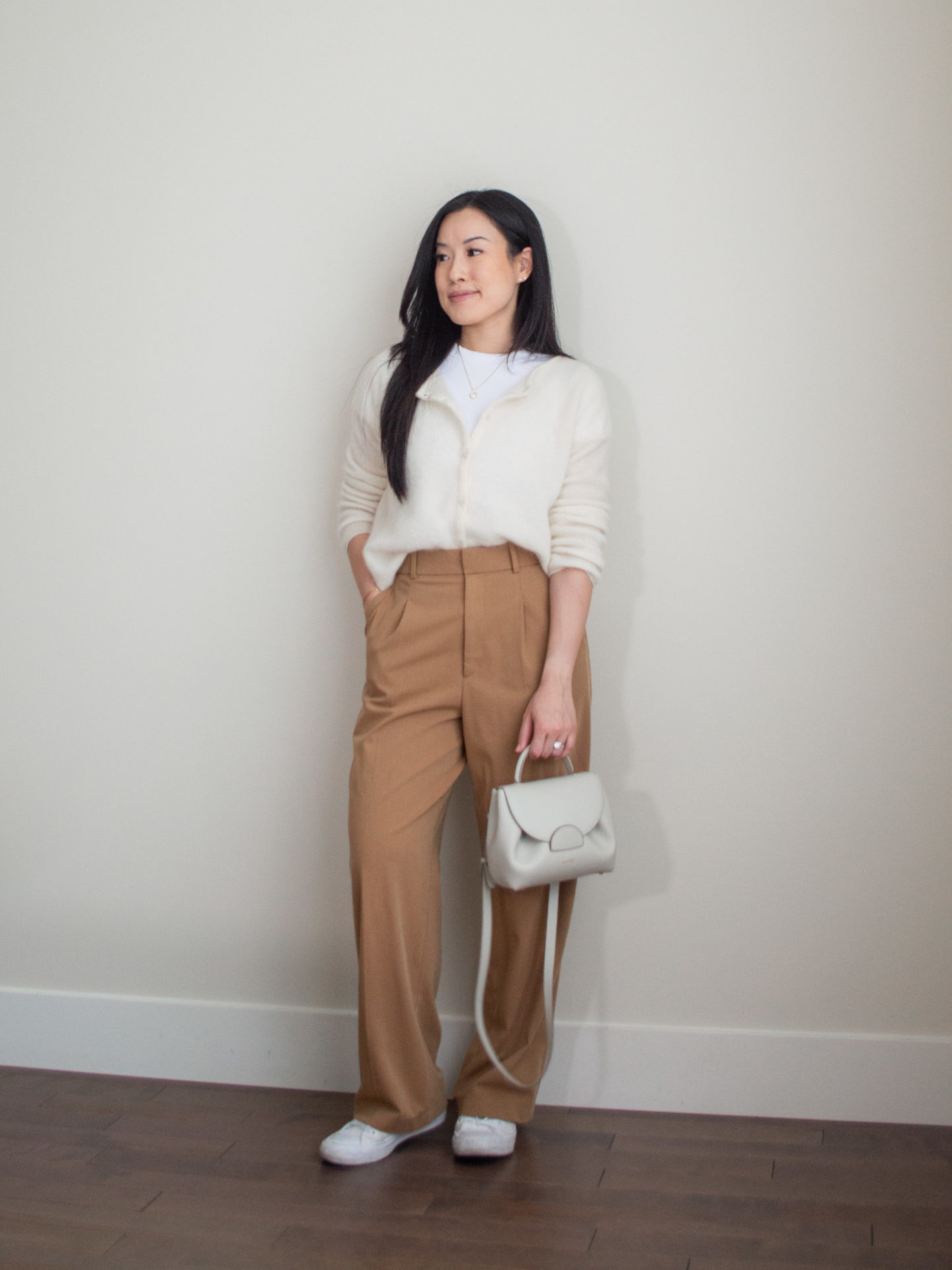 Sharon of Her Simple Sole is showcasing an outfit inspired by Parisian style, featuring a basic white T-Shirt, cream button-up cardigan, brown wide-leg pants, an off-white crossbody bag and white sneakers | minimalist outfits | fall outfit ideas | simple outfit ideas