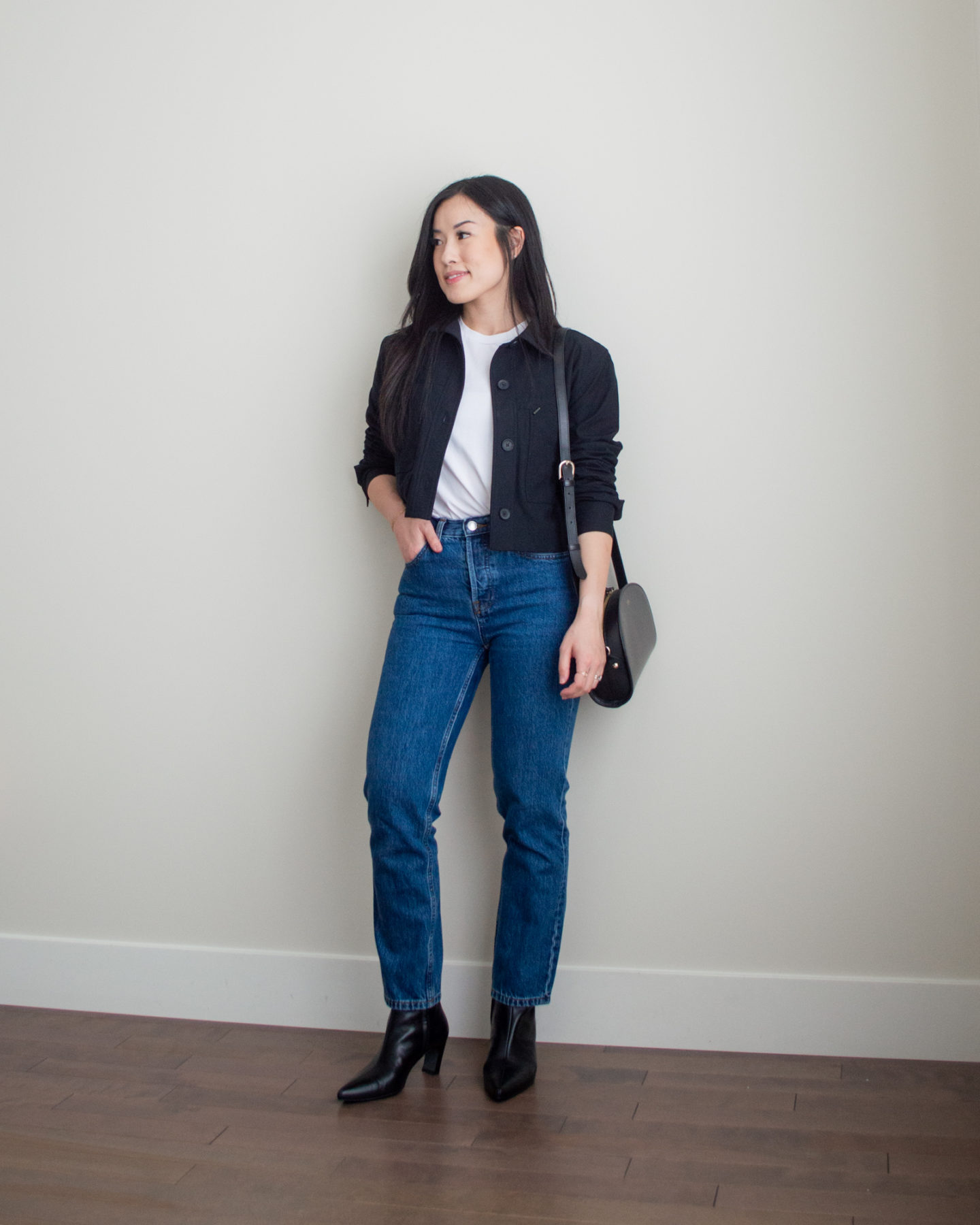 Sharon of Her Simple Sole is showcasing an outfit from her September outfit roundup, featuring a basic white T-Shirt, black cropped jacket, blue straight leg jeans, a black crossbody bag and black pointy toe ankle boots | minimalist outfits | simple outfit ideas