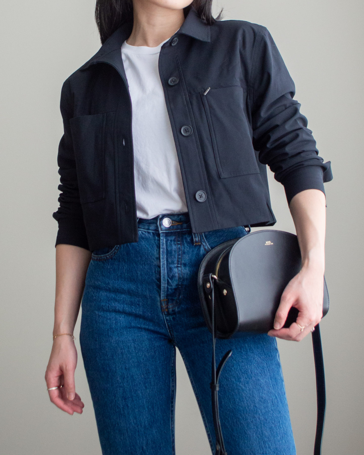 Close-up detailed outfit shot of Sharon of Her Simple Sole wearing a basic white T-Shirt, black cropped jacket, dark blue straight-leg jeans, and a black half moon crossbody bag | minimalist outfits | simple outfit ideas