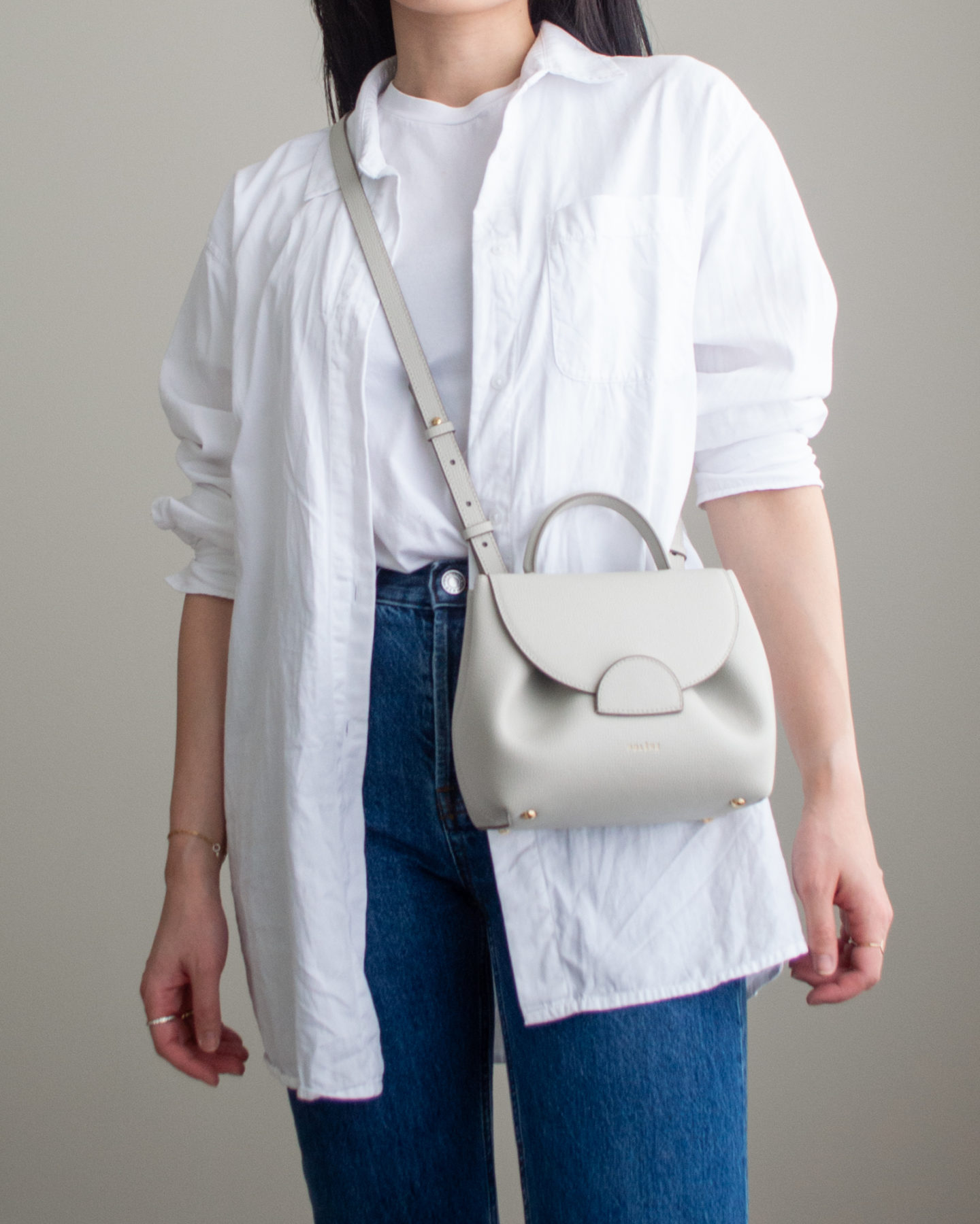 Close-up detailed outfit shot of Sharon of Her Simple Sole wearing a basic white T-Shirt, an oversized white button-up shirt, dark blue straight leg jeans, an off-white crossbody bag | minimalist outfits | simple outfit ideas