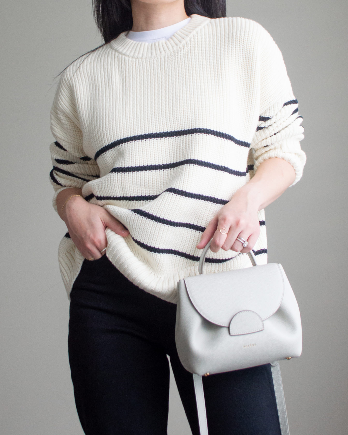 Close-up detailed outfit shot of Sharon of Her Simple Sole wearing a basic white T-Shirt, a striped cotton sweater, black straight leg jeans, and an off-white crossbody bag | minimalist outfits | simple outfit ideas