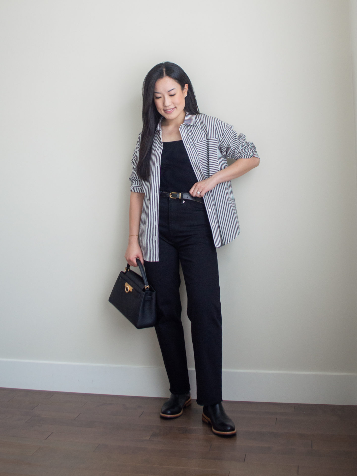 Sharon of Her Simple Sole is showcasing an outfit from her September outfit roundup, featuring a black square neck tank top, a striped button-up shirt, black straight leg jeans, a black top handle bag and black Chelsea boots | minimalist outfits | simple outfit ideas