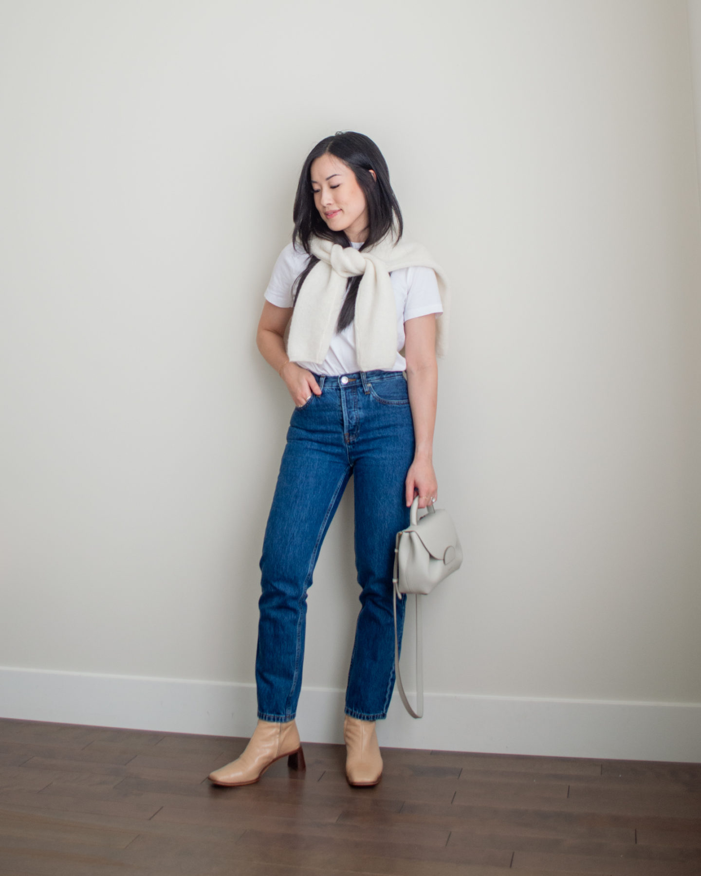 Sharon of Her Simple Sole is showcasing an outfit from her September outfit roundup, featuring a basic white T-Shirt, blue straight leg jeans, a wool cardigan over the shoulders, an off-white crossbody bag and nude ankle boots | minimalist outfits | simple outfit ideas