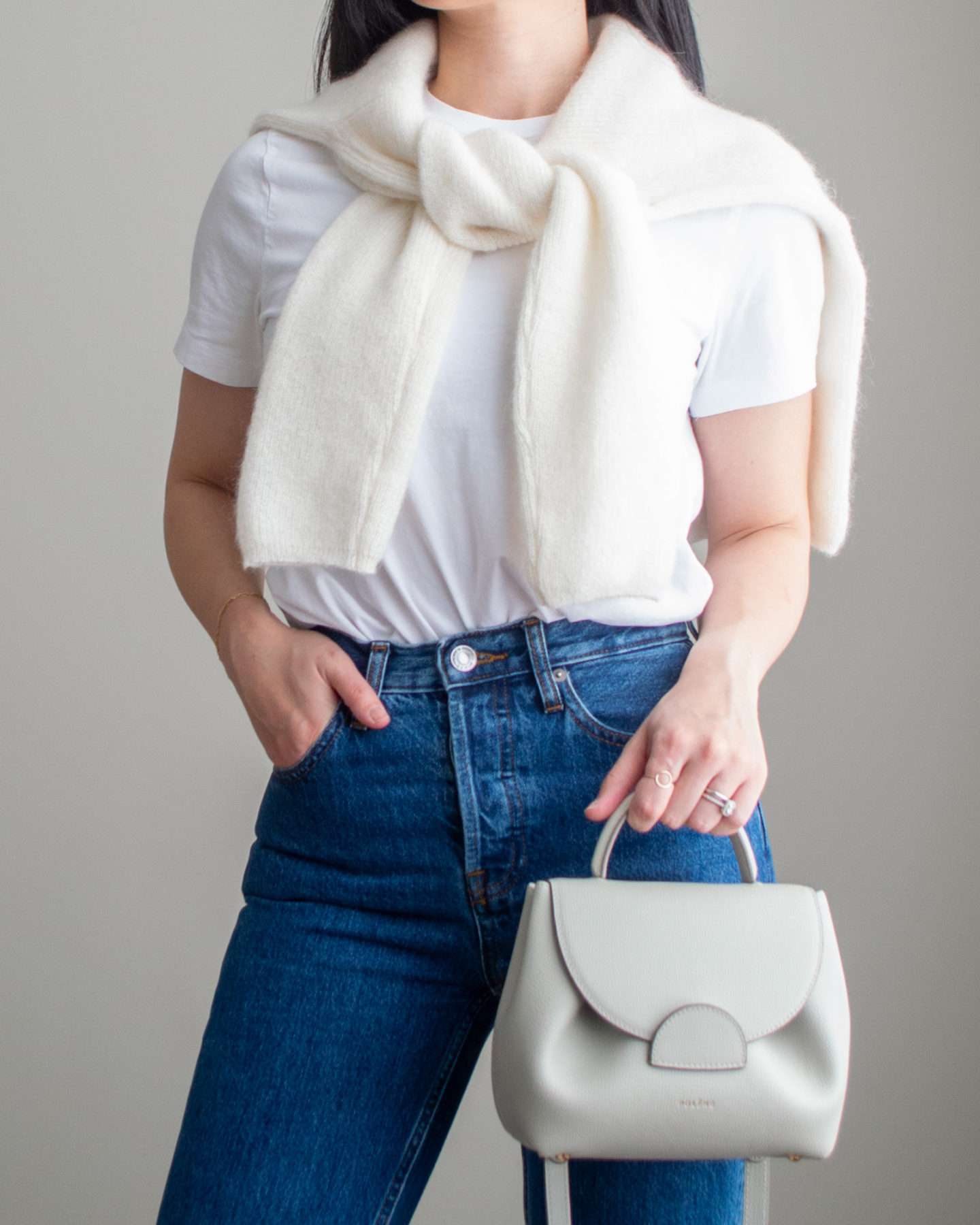 Close-up detailed outfit shot of Sharon of Her Simple Sole wearing a basic white T-Shirt, blue straight leg jeans, a wool cardigan over the shoulders, an off-white crossbody bag | minimalist outfits | simple outfit ideas