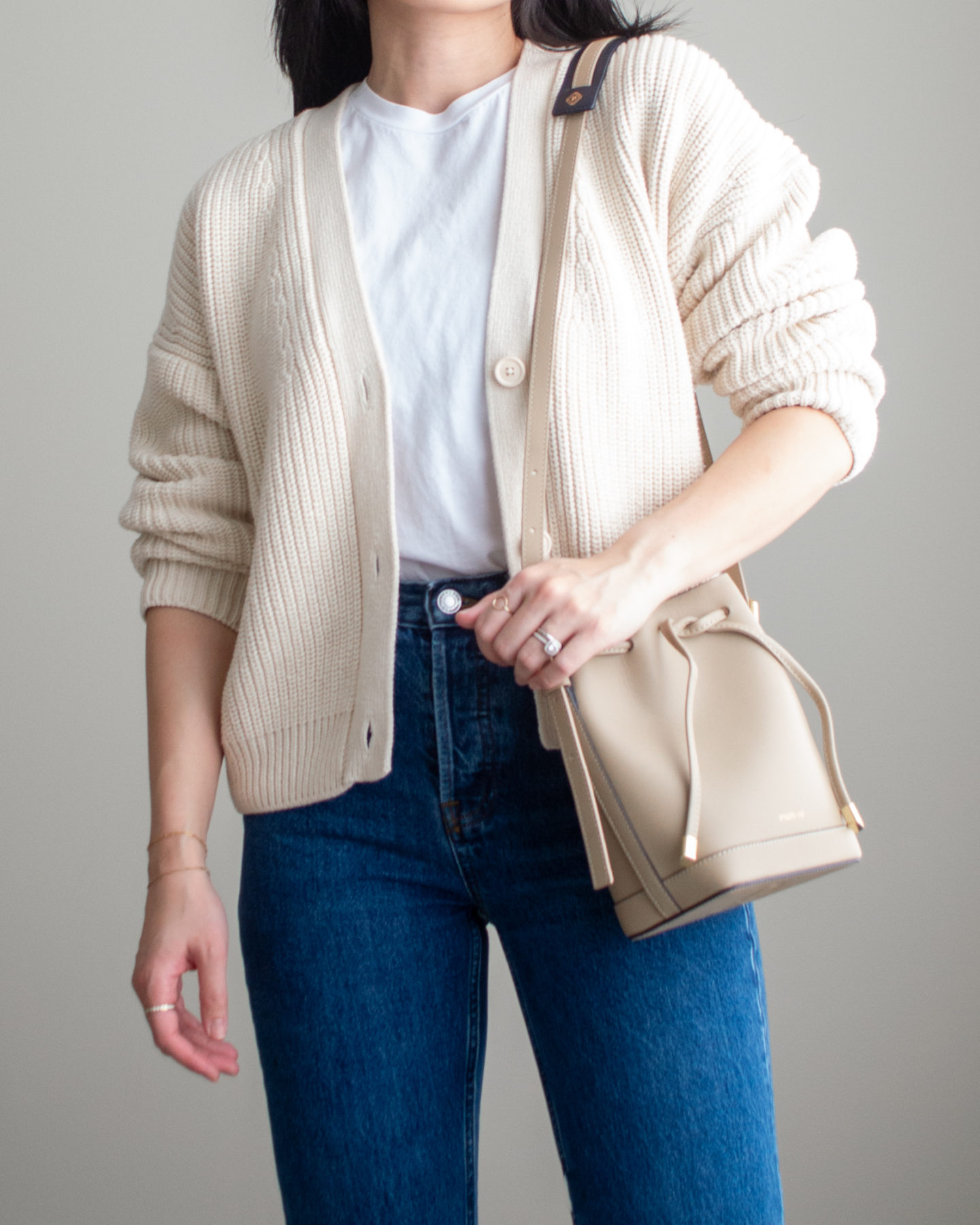 Close-up detailed outfit shot of Sharon of Her Simple Sole wearing a basic white T-Shirt, blue straight leg jeans, a cream cardigan, and a taupe bucket bag | minimalist outfits | simple outfit ideas