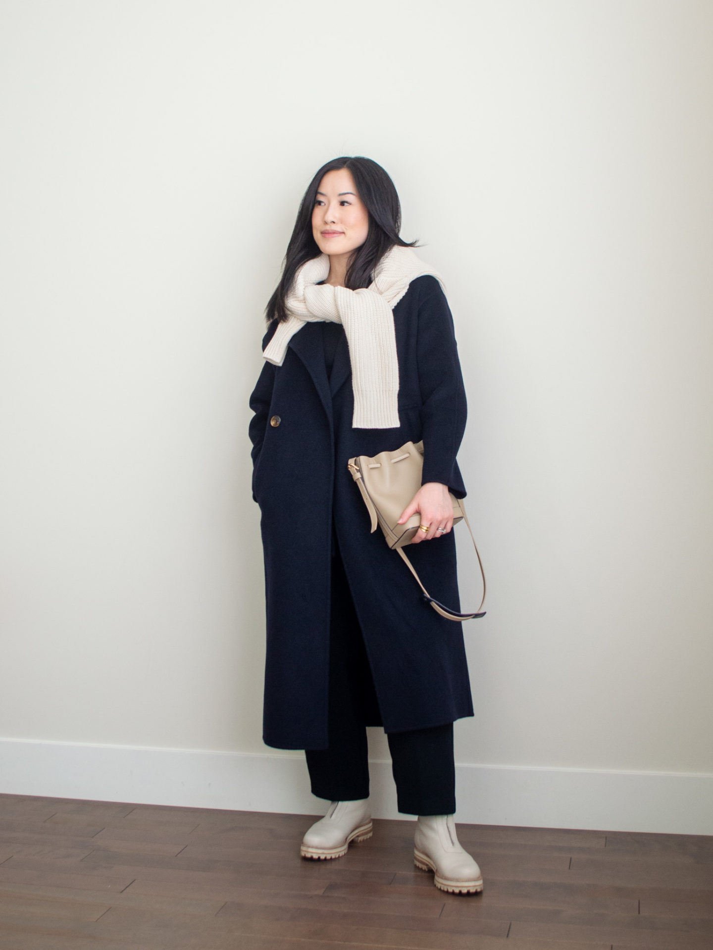 Sharon of Her Simple Sole is showcasing 1 of 10 fall outfits featuring a navy cashmere coat, cream cotton cardigan over the shoulders, black long sleeve top, black cropped trousers, taupe bucket bag and cream chunky boots | minimalist outfits | simple outfit ideas | easy fall outfit