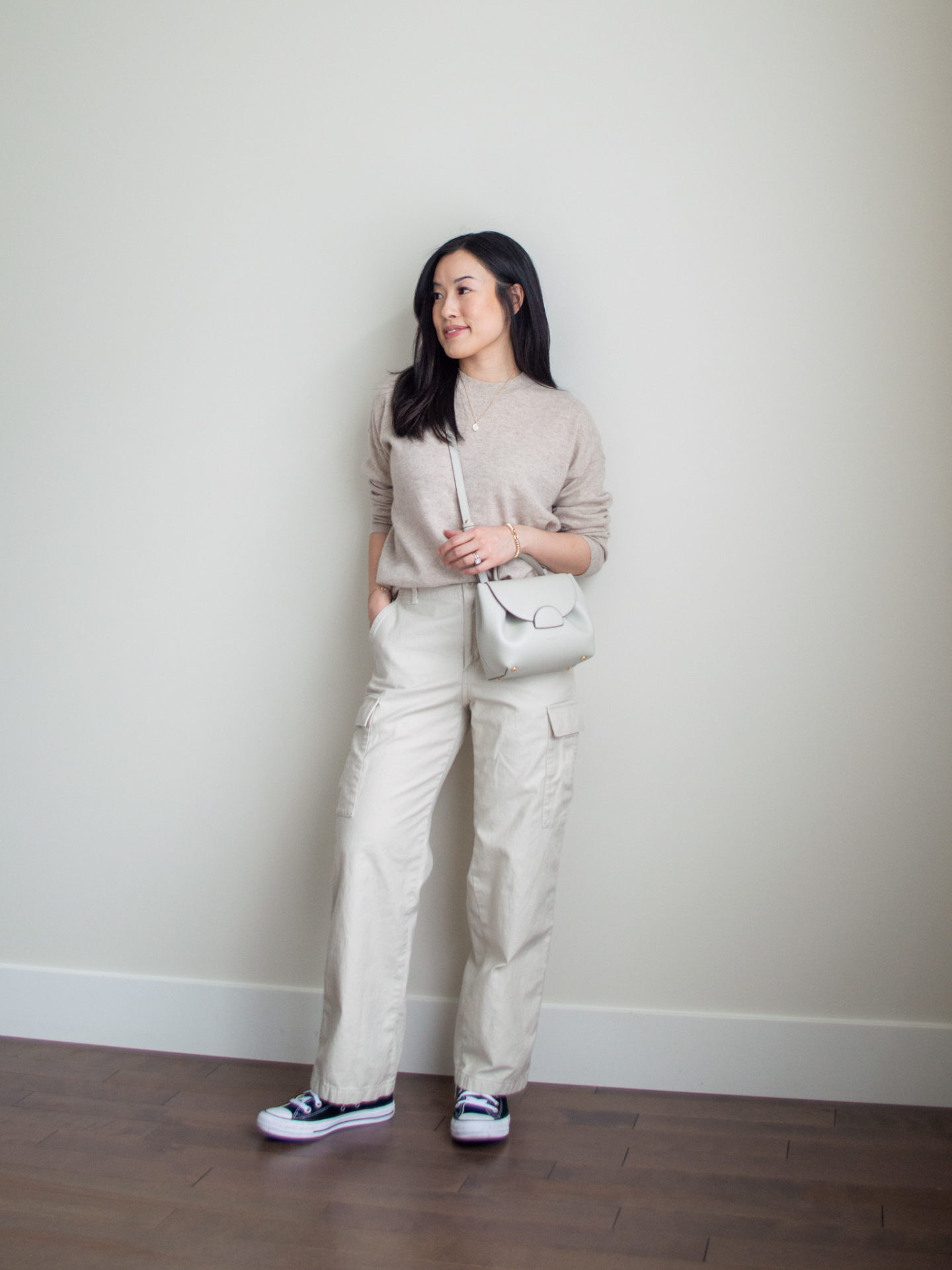 Sharon of Her Simple Sole is showcasing an outfit from a weekend trip in a backpack featuring a beige cashmere sweater, cream cargo pants, black Converse sneakers, and an off-white crossbody bag | minimalist outfits | fall outfit ideas | simple outfit ideas