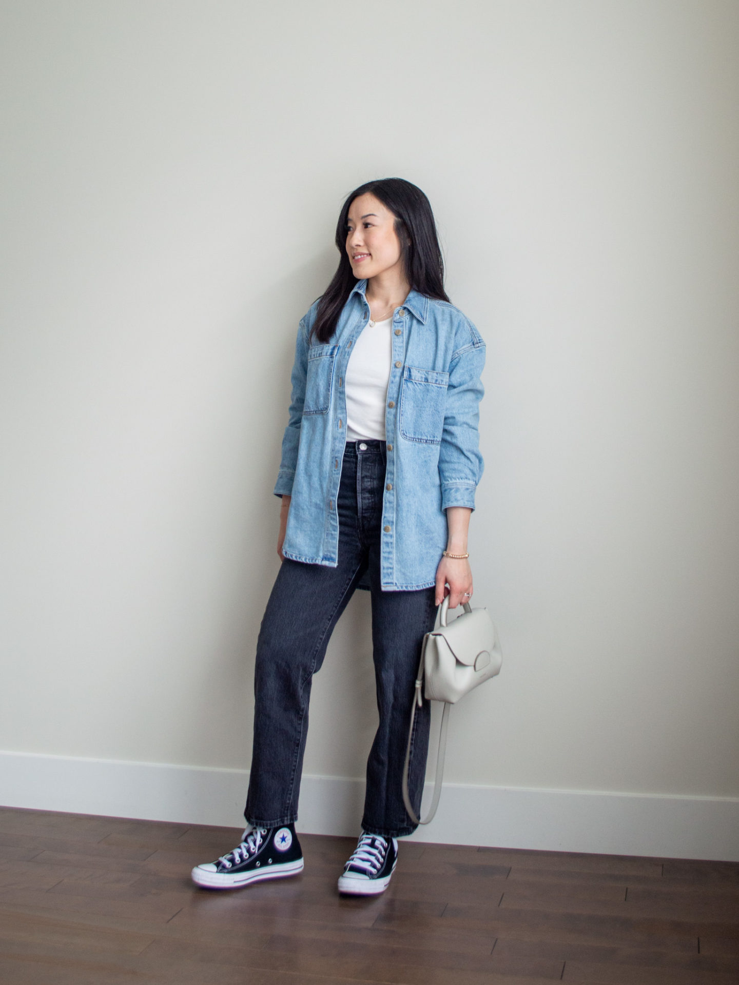 Sharon of Her Simple Sole is showcasing an outfit from a weekend trip in a backpack featuring an oversized denim jacket, white long sleeve shirt, grey straight leg jeans, black Converse sneakers and an off-white crossbody bag | minimalist outfits | fall outfit ideas | simple outfit ideas