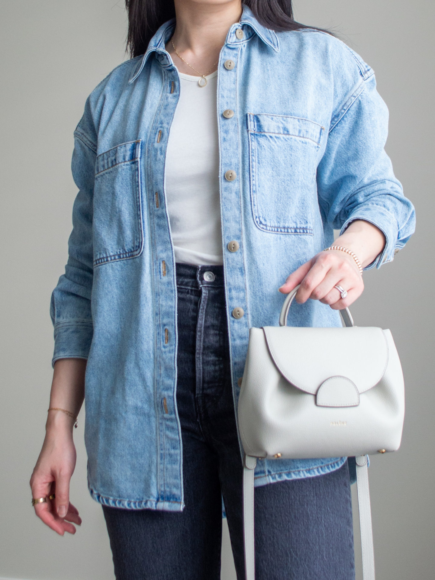 Close-up detailed outfit shot of Sharon of Her Simple Sole wearing an oversized denim jacket, white long sleeve shirt, grey straight leg jeans, and an off-white crossbody bag | minimalist outfits | simple outfit ideas