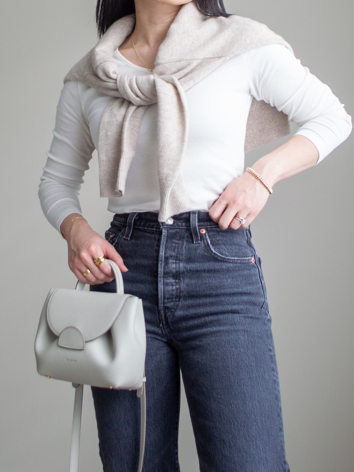 Close-up detailed outfit shot of Sharon of Her Simple Sole wearing a white long sleeve shirt, a beige cashmere sweater over the shoulders, grey straight leg jeans and an off-white crossbody bag | minimalist outfits | simple outfit ideas