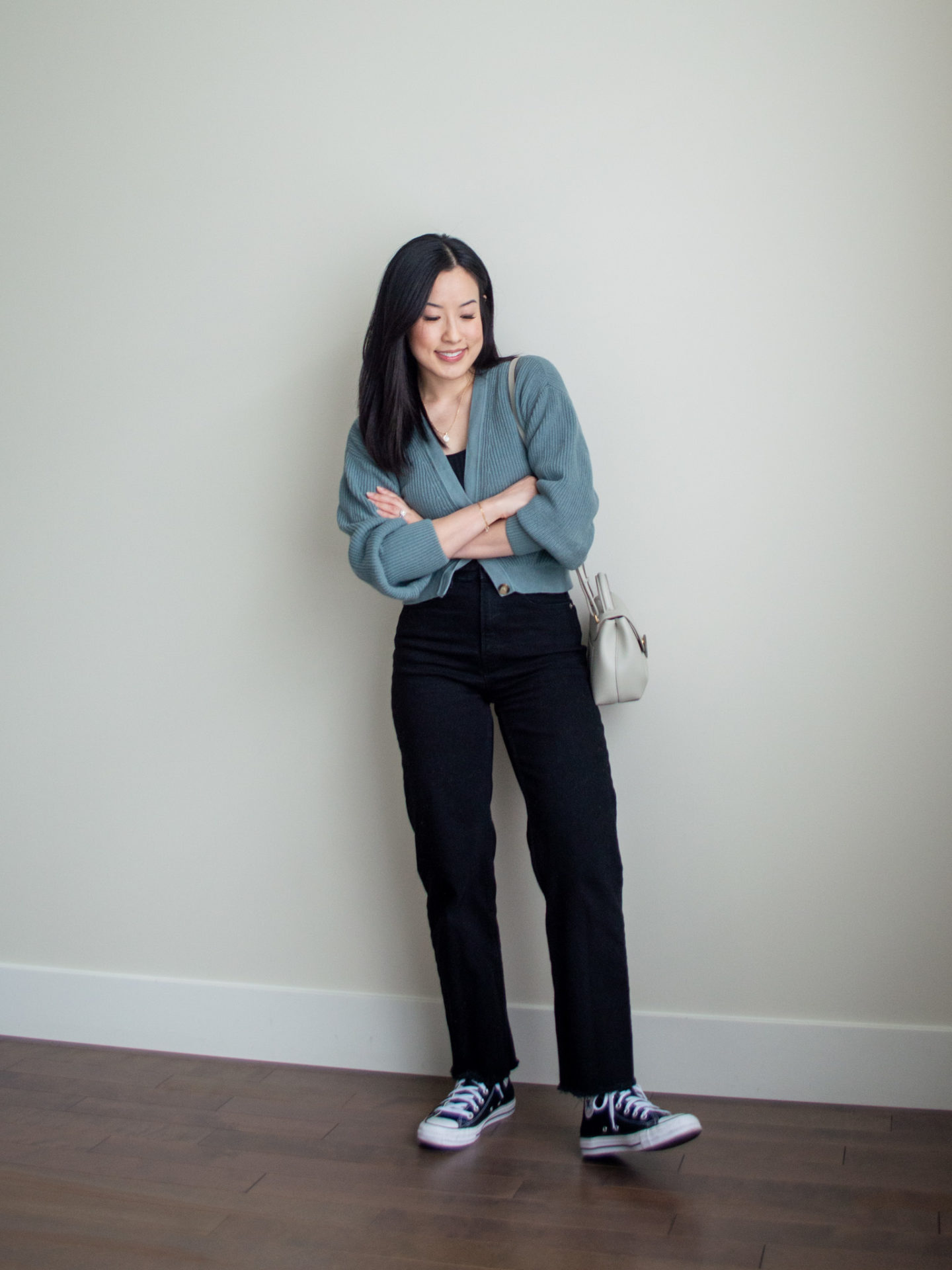 Sharon of Her Simple Sole is showcasing an outfit from a weekend trip in a backpack featuring a black ribbed tank top, a cropped cardigan, black straight leg jeans, black Converse sneakers and an off-white crossbody bag | minimalist outfits | fall outfit ideas | simple outfit ideas